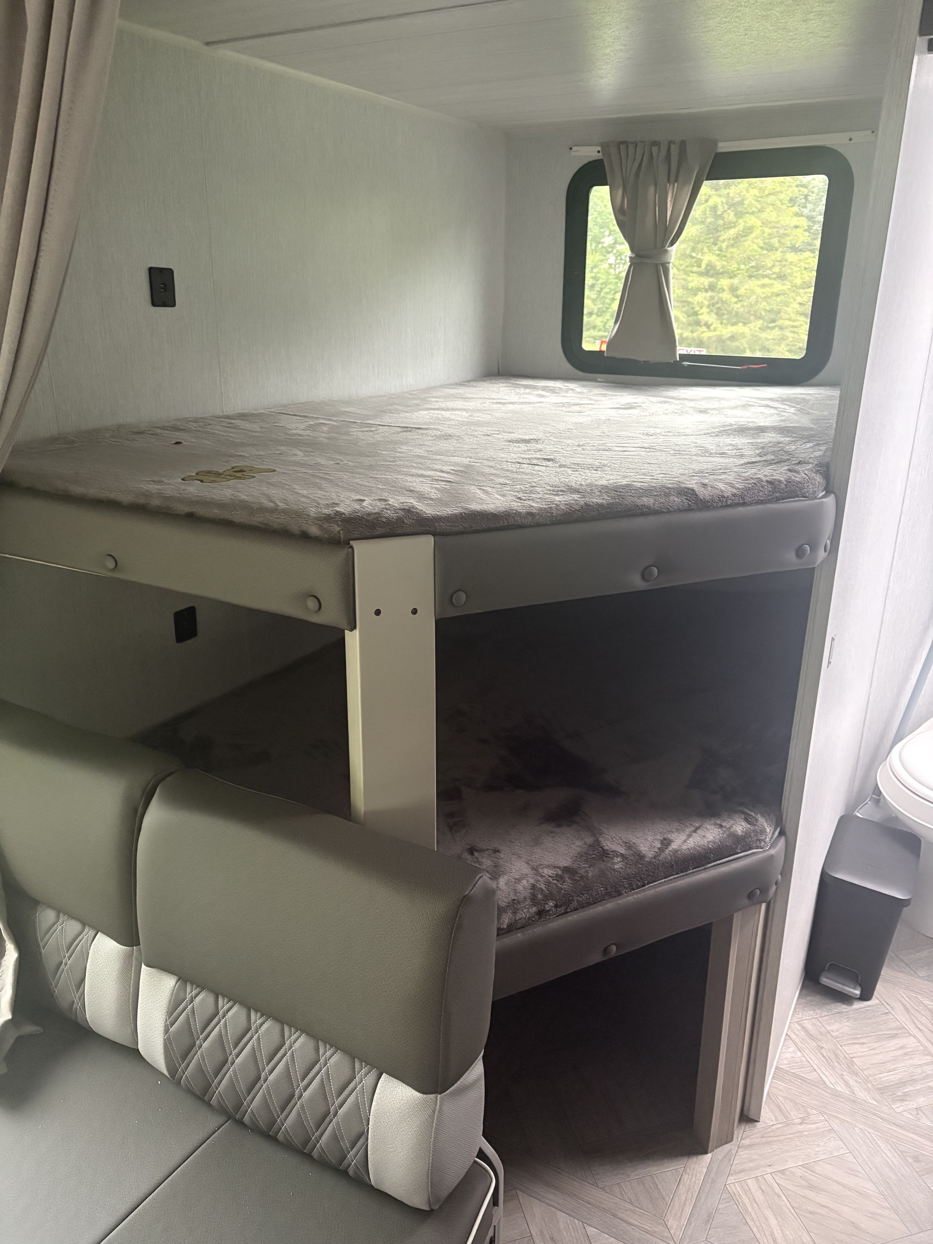 An RV rental interior showing bunk beds with a yellow stain on the top bunk, a window view, and seating.. Forest River Wildwood X-Lite 2023