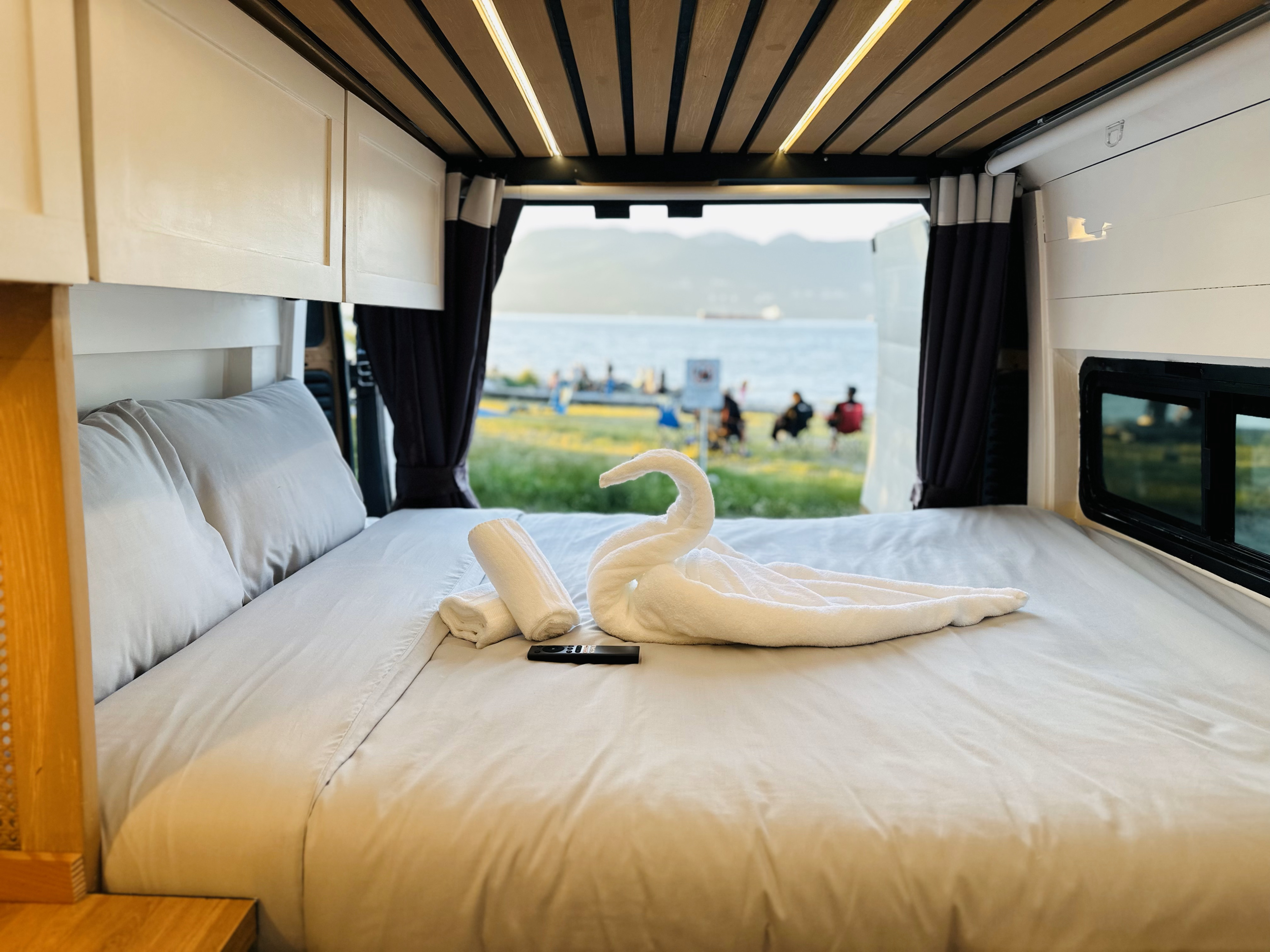 Cozy RV rental's bed with swan towel, offering serene water & mountain views for your mobile escape.. Dodge Promaster 3500 2016