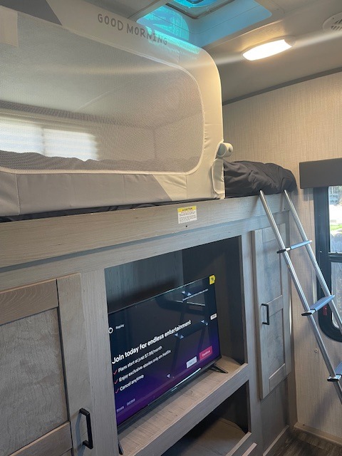 Inside an RV rental: a cozy bunk with a 'Good Morning' safety net, and a TV below. Ideal for family travel, offering comfort and entertainment.. Heartland RVs Mallard 2021