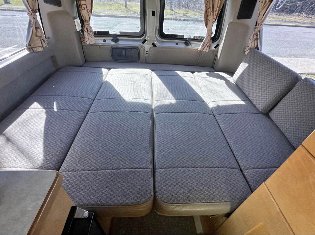 Spacious RV rental interior showing a versatile grey upholstered bed/seating area with windows.. Chevrolet chevrolet express 2500 New West high 2004