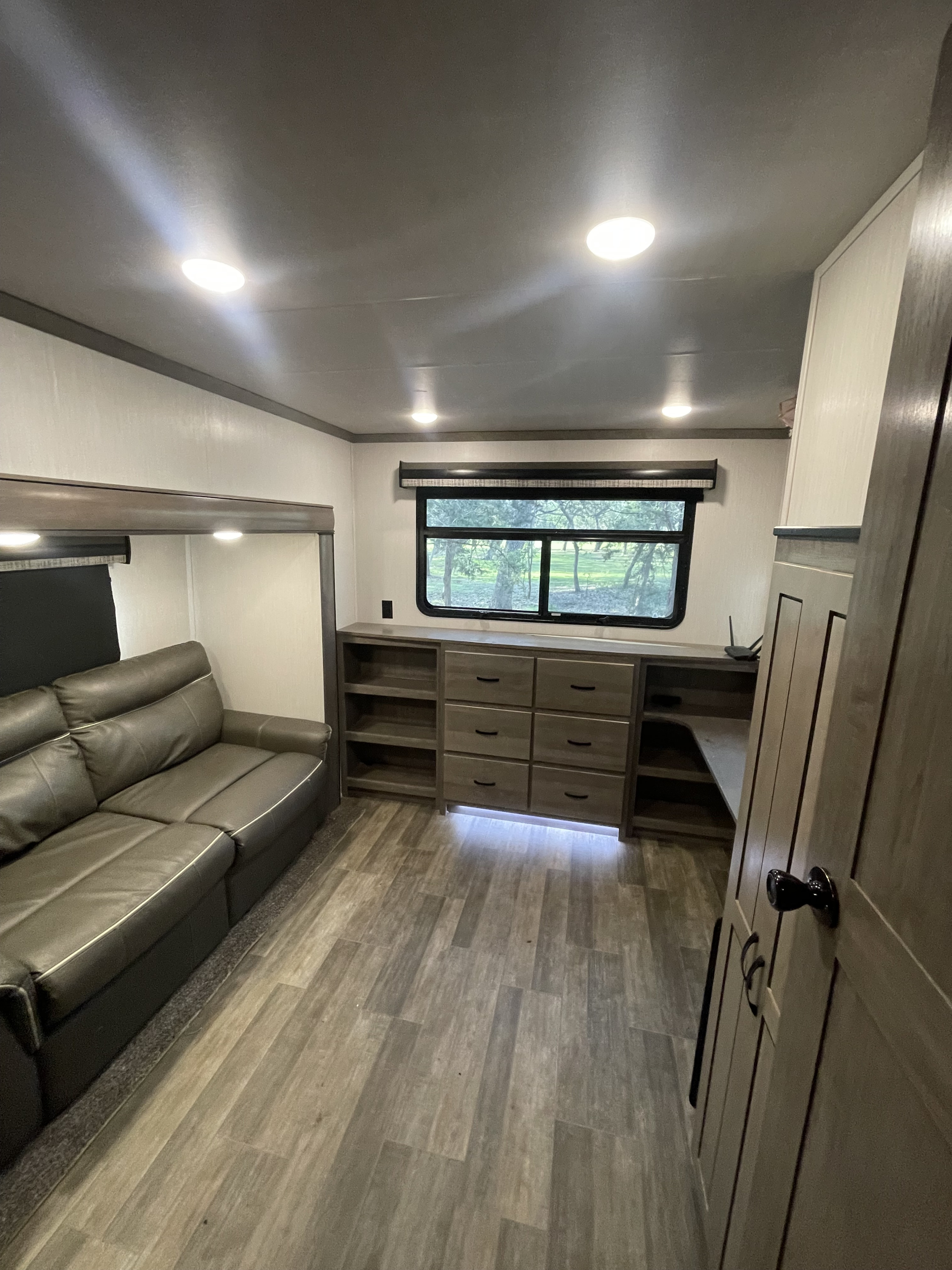 This RV rental offers a modern living space with a comfy dark grey sofa, built-in storage, and a bright window.. Cedar Creek Cedar Creek Fifth Wheel 2021