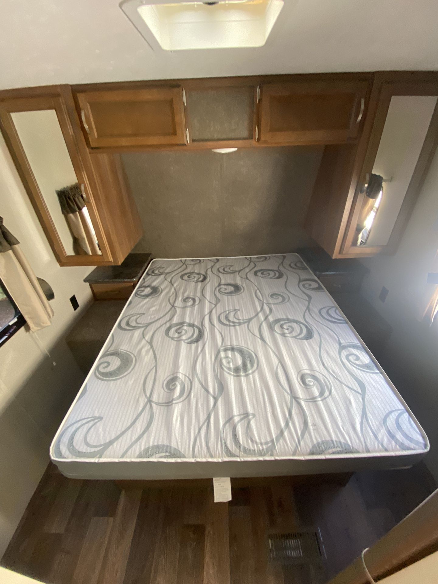 RV rental bedroom: Features a queen bed with patterned mattress, wood laminate floor, and overhead storage cabinets.. Keystone RV Springdale 2015