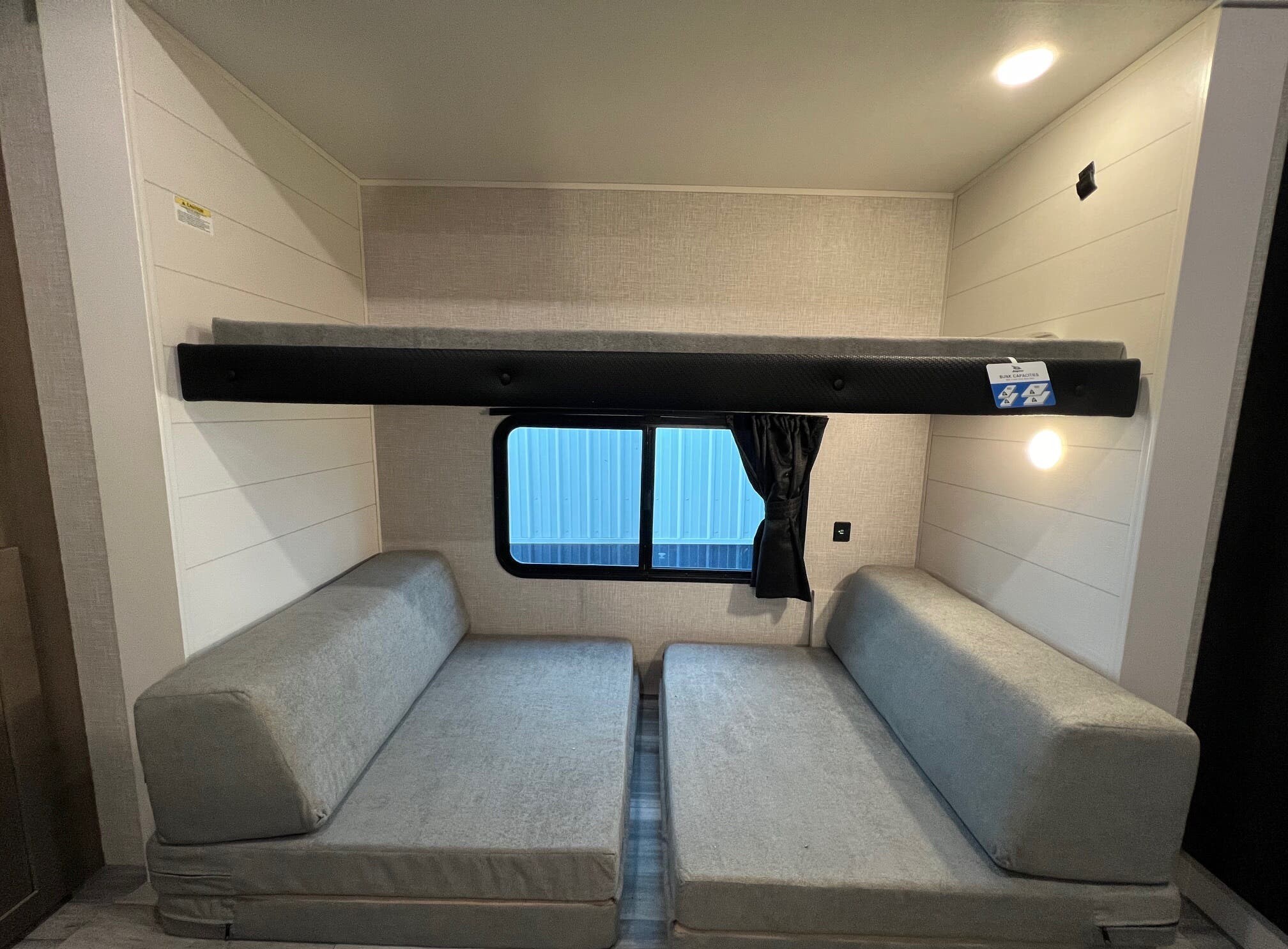 RV rental interior: an upper bunk bed over two lower gray cushion beds/seating, next to a window.. 1UJBC0BT8S1YT0519 321BDS 2025