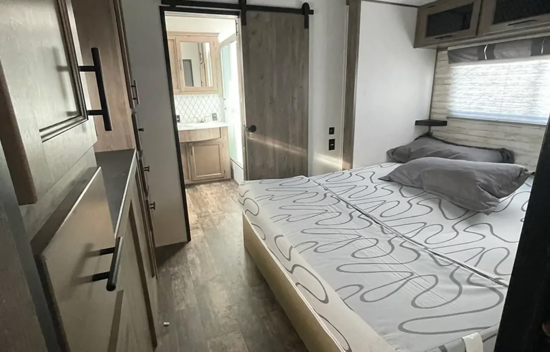 Modern RV rental interior: bedroom with bed, storage, and en-suite bathroom via sliding door. Ideal compact living.. Forest River Sabre 2021