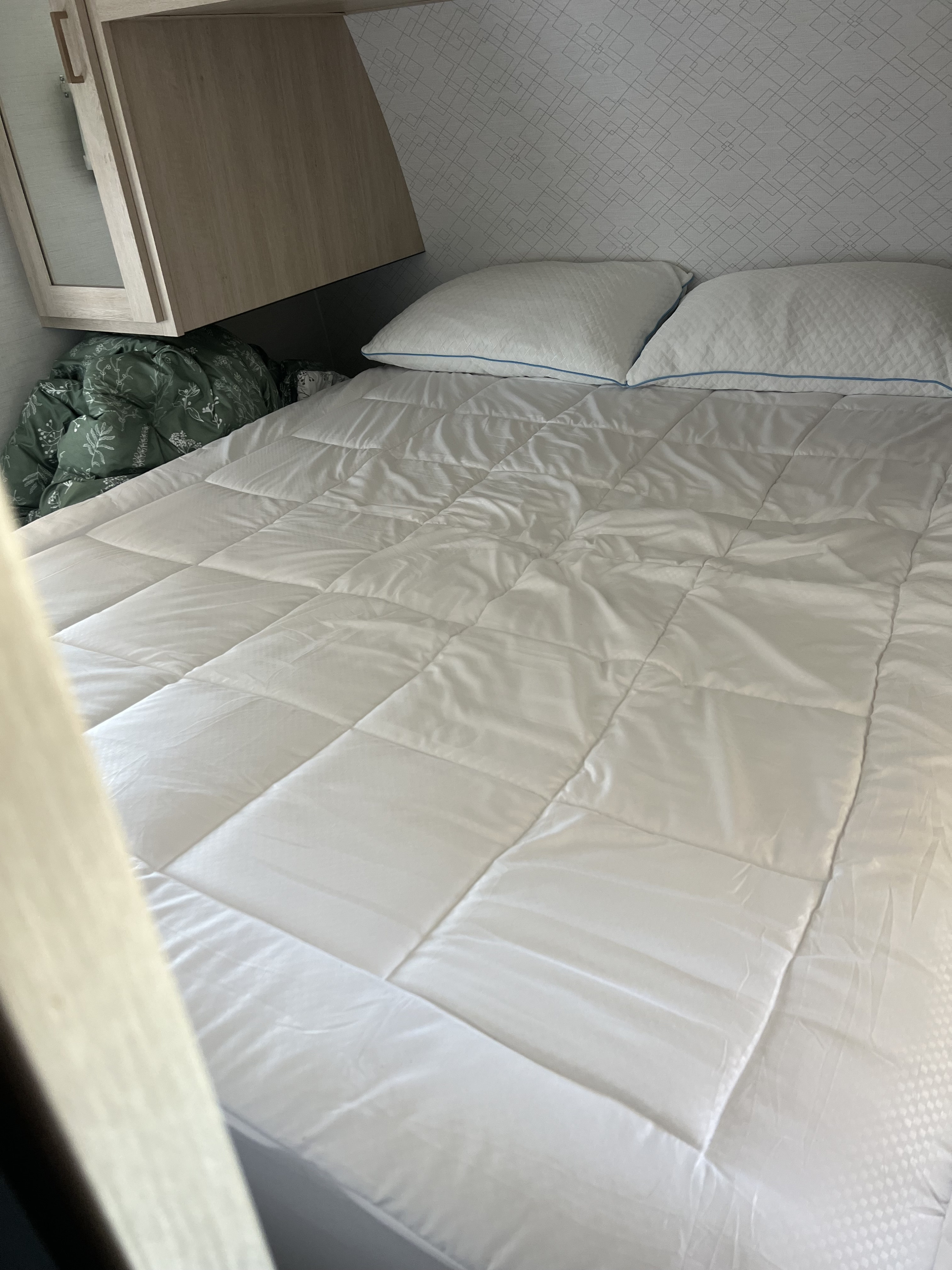 Clean, cozy RV rental bed with a white quilted comforter and pillows under wood-toned cabinets, perfect for travel.. Prime Time 26dbsle 2024