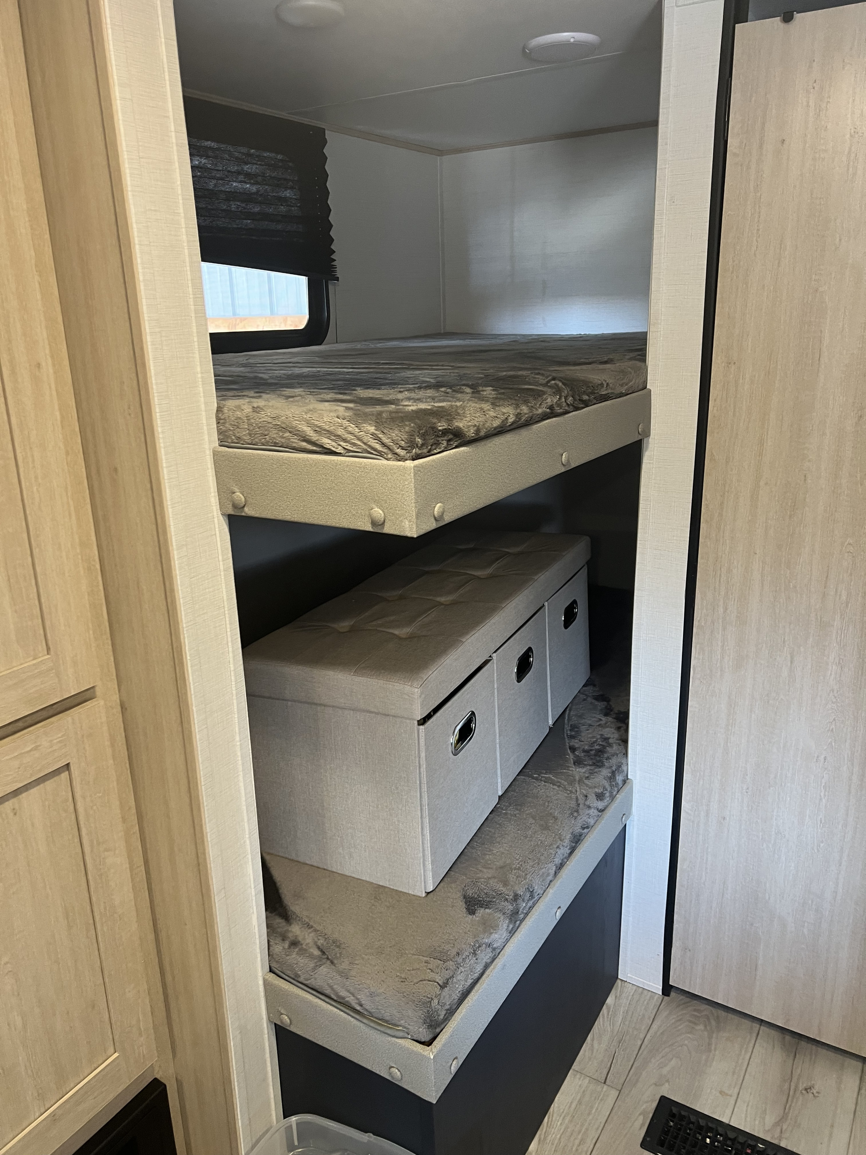 RV rental bunk beds are shown, featuring a window, comfortable bedding, and a storage ottoman below. Practical design.. Prime Time 26dbsle 2024