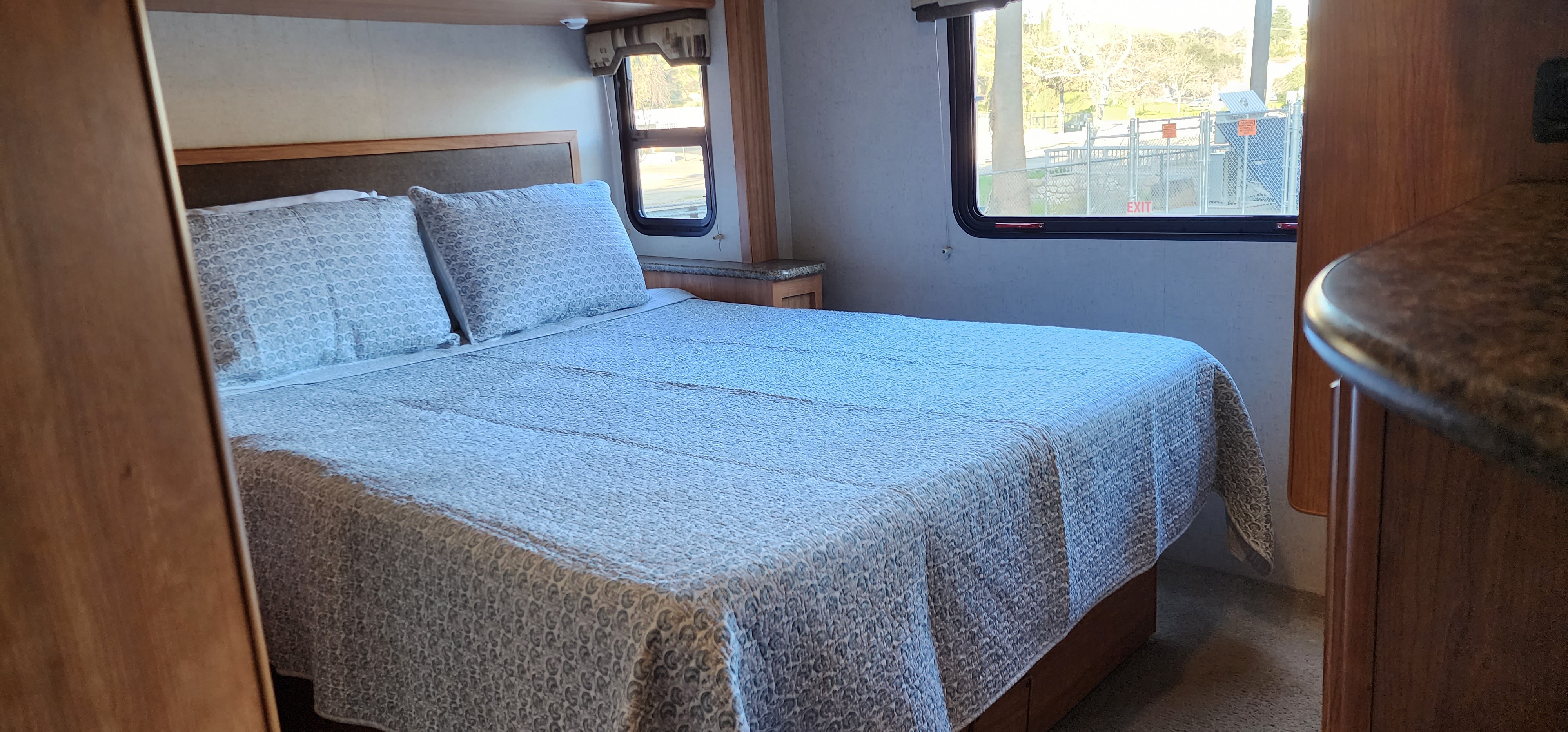 Explore this inviting RV rental bedroom. It features a cozy bed with patterned linens, wood cabinetry, and outdoor views.. Jamboree Sport 2010