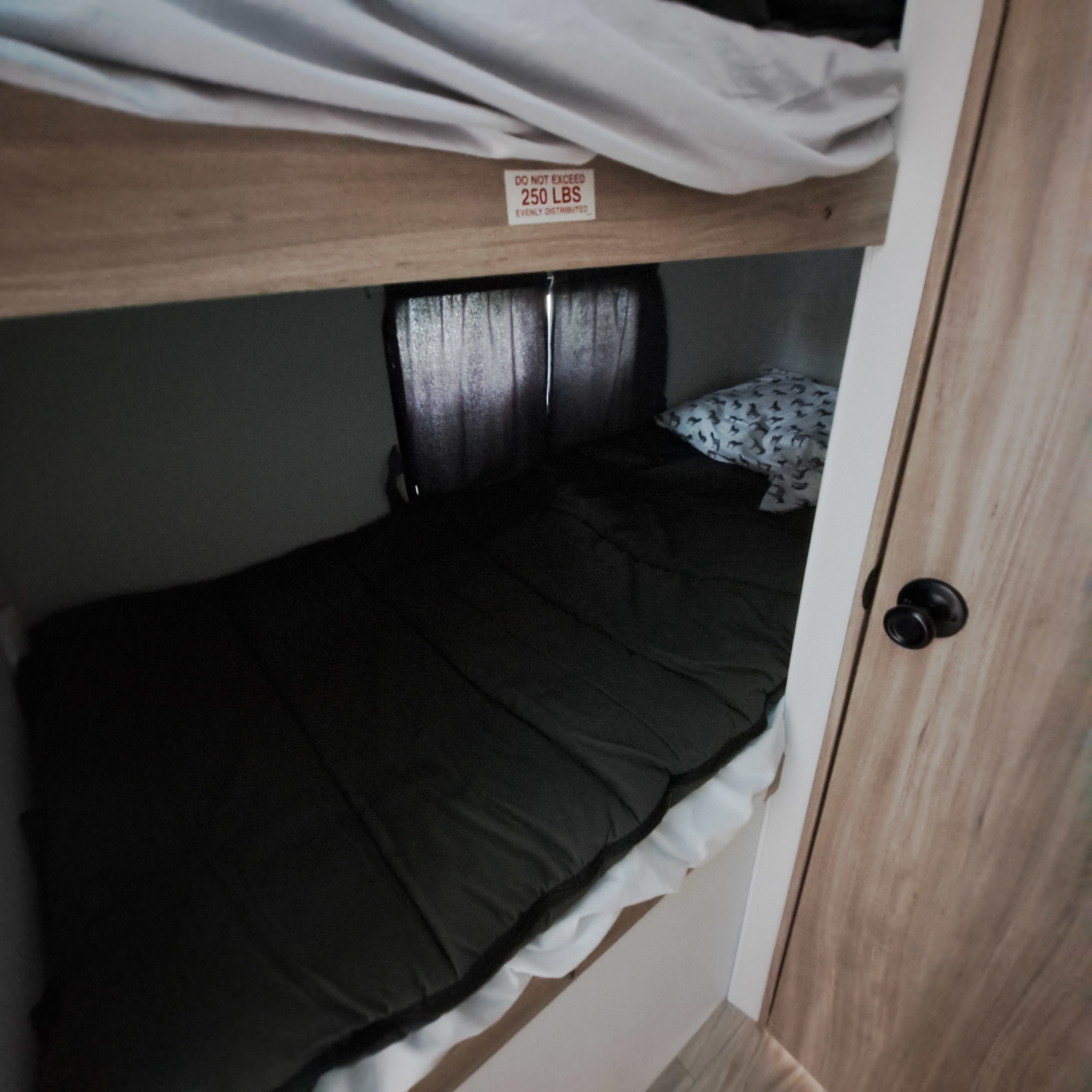 Compact bunk beds in an RV rental, with a dark sleeping bag on the lower bunk and a 250 lbs weight limit sign on the top bunk.. Winnebago Access 26BH 2025