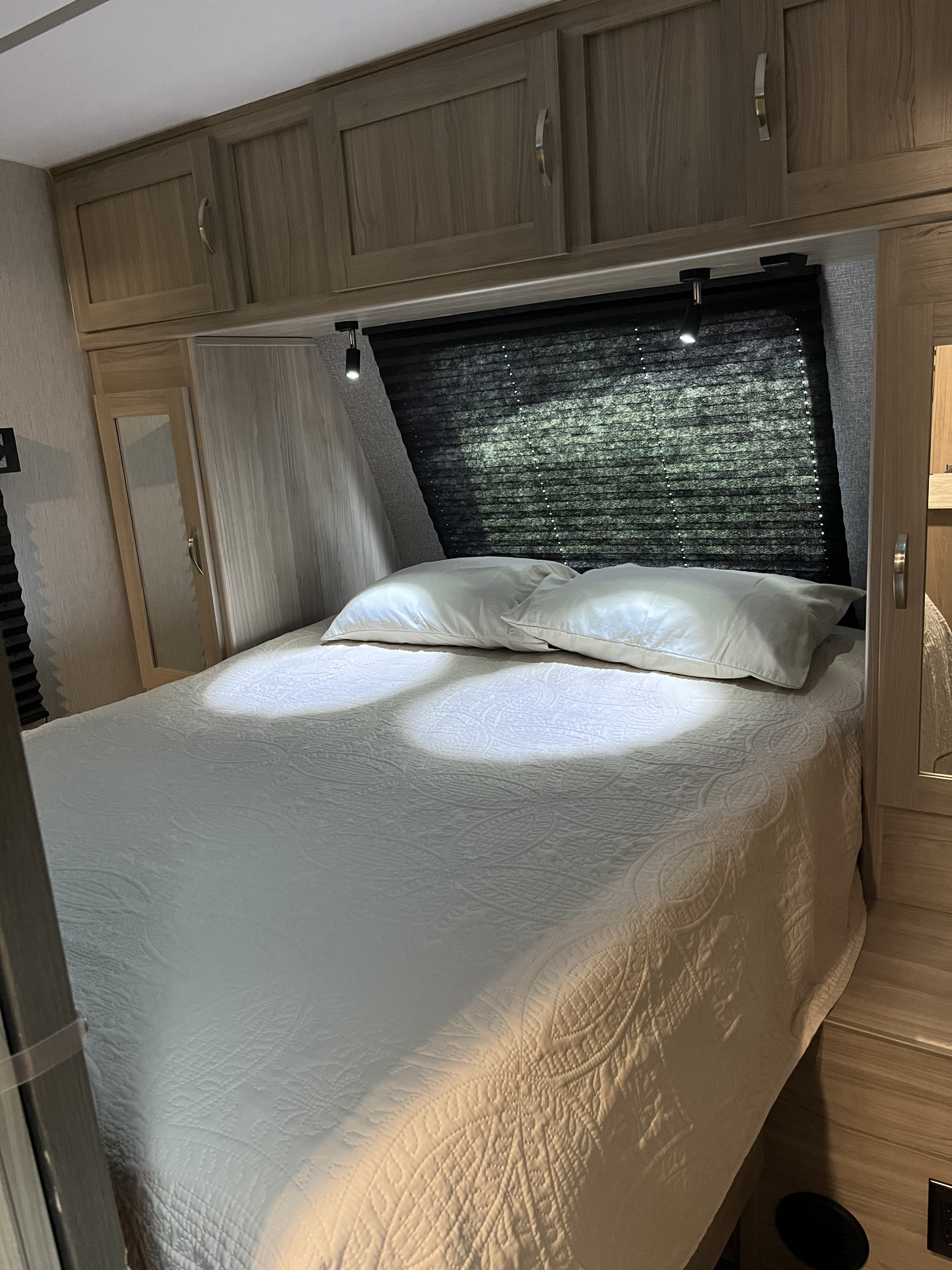 Inside an RV rental: a compact bedroom with a white quilted bed, reading lights, and ample overhead storage.. Coachmen Freedom Express Ultra Lite 292BHDS 2021