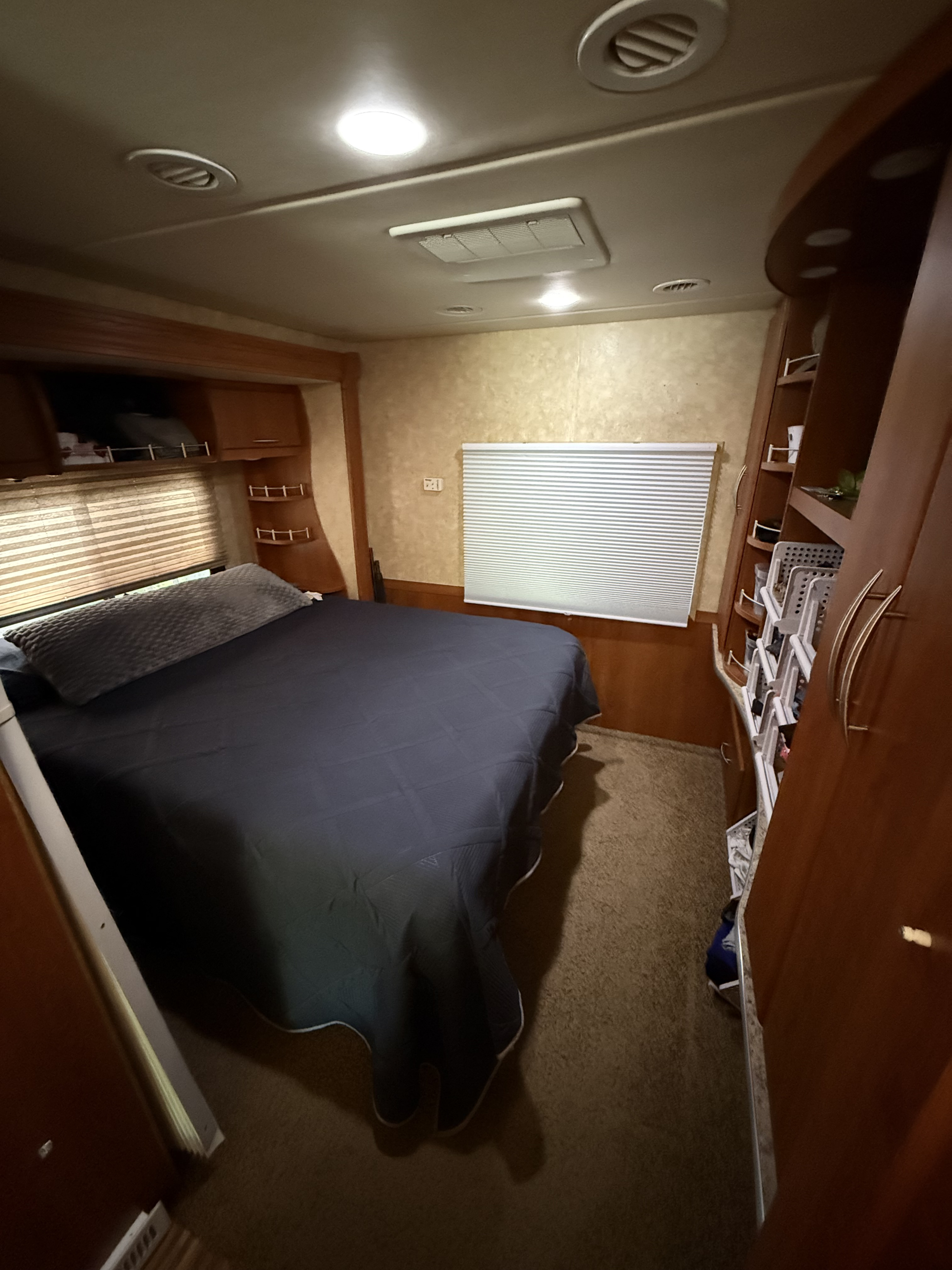 Cozy RV rental bedroom featuring a comfortable bed, overhead storage, window blinds, and built-in shelving and cabinets.. Coachmen Mirada 2009