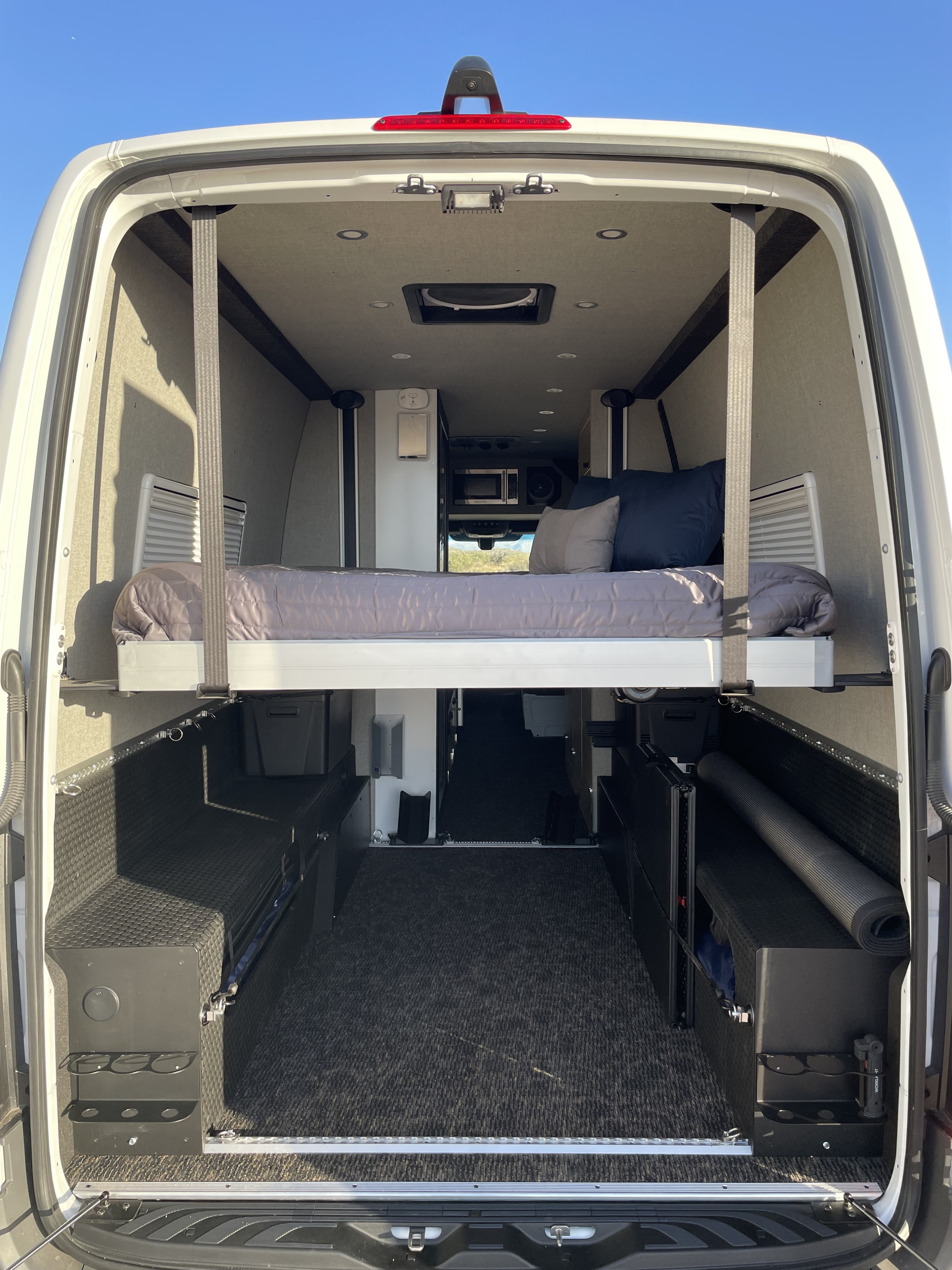RV rental: Spacious camper van interior with an elevated bed, large storage area, and modern amenities.. Mercedes Sprinter 2023