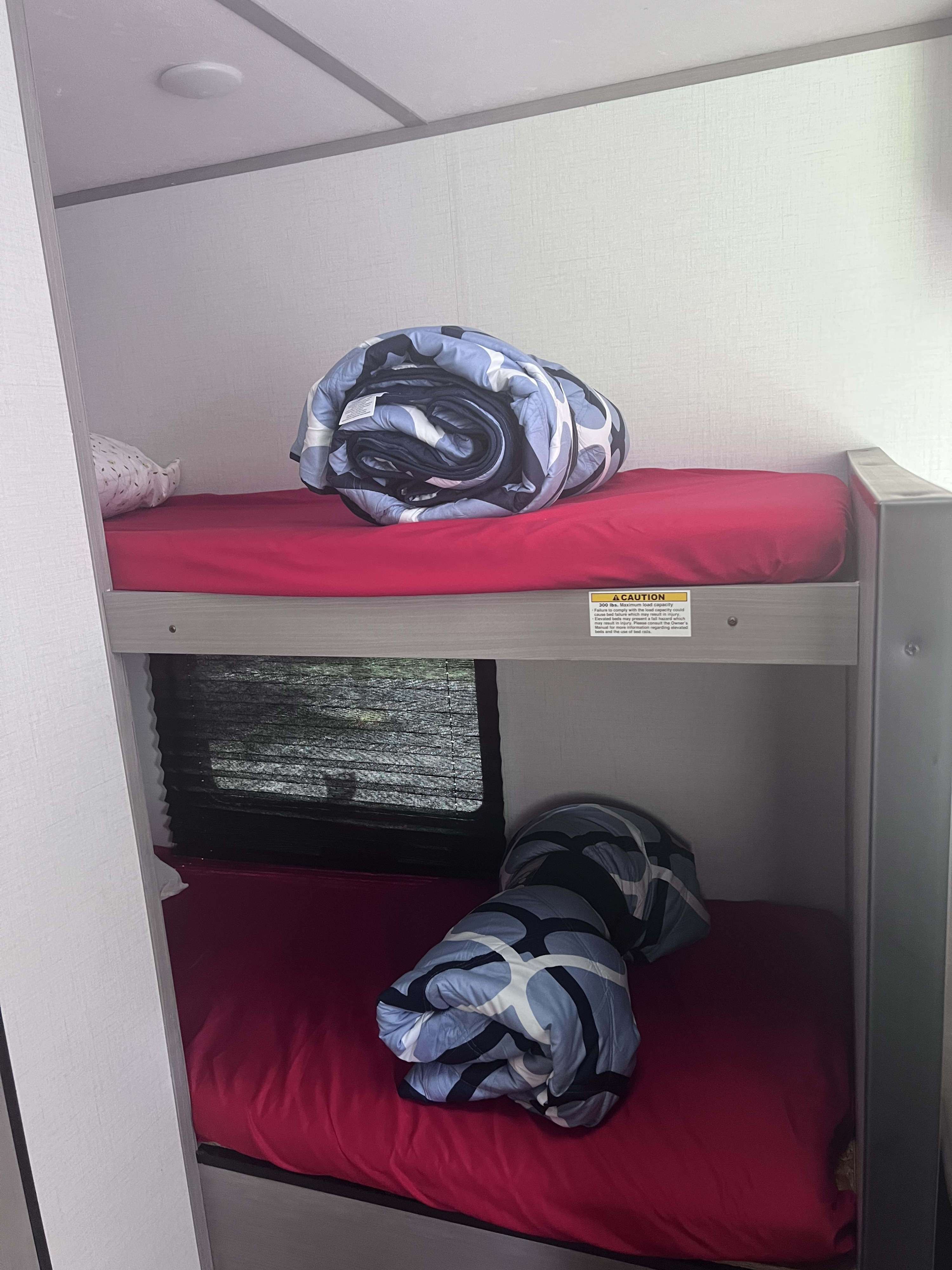 RV rental bunk beds with red sheets & rolled blankets, showing a caution label. Perfect for family trips.. Keystone RV 4YDTCMG1XRM931201 2023