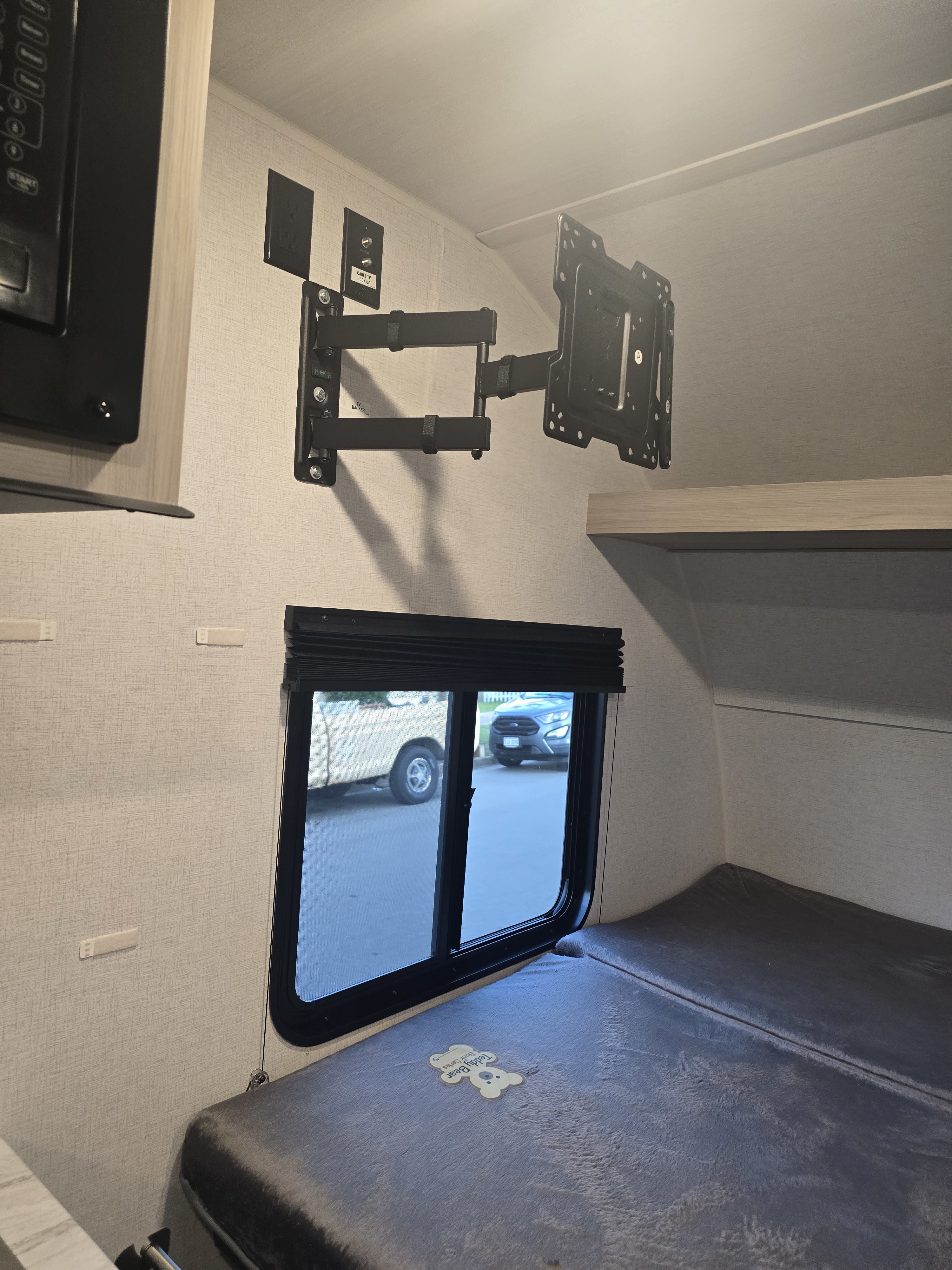 Inside an **RV rental**: a comfortable bunk bed, window with outdoor view, and TV mount with power outlets.. East to West Silver Lake LE 2024