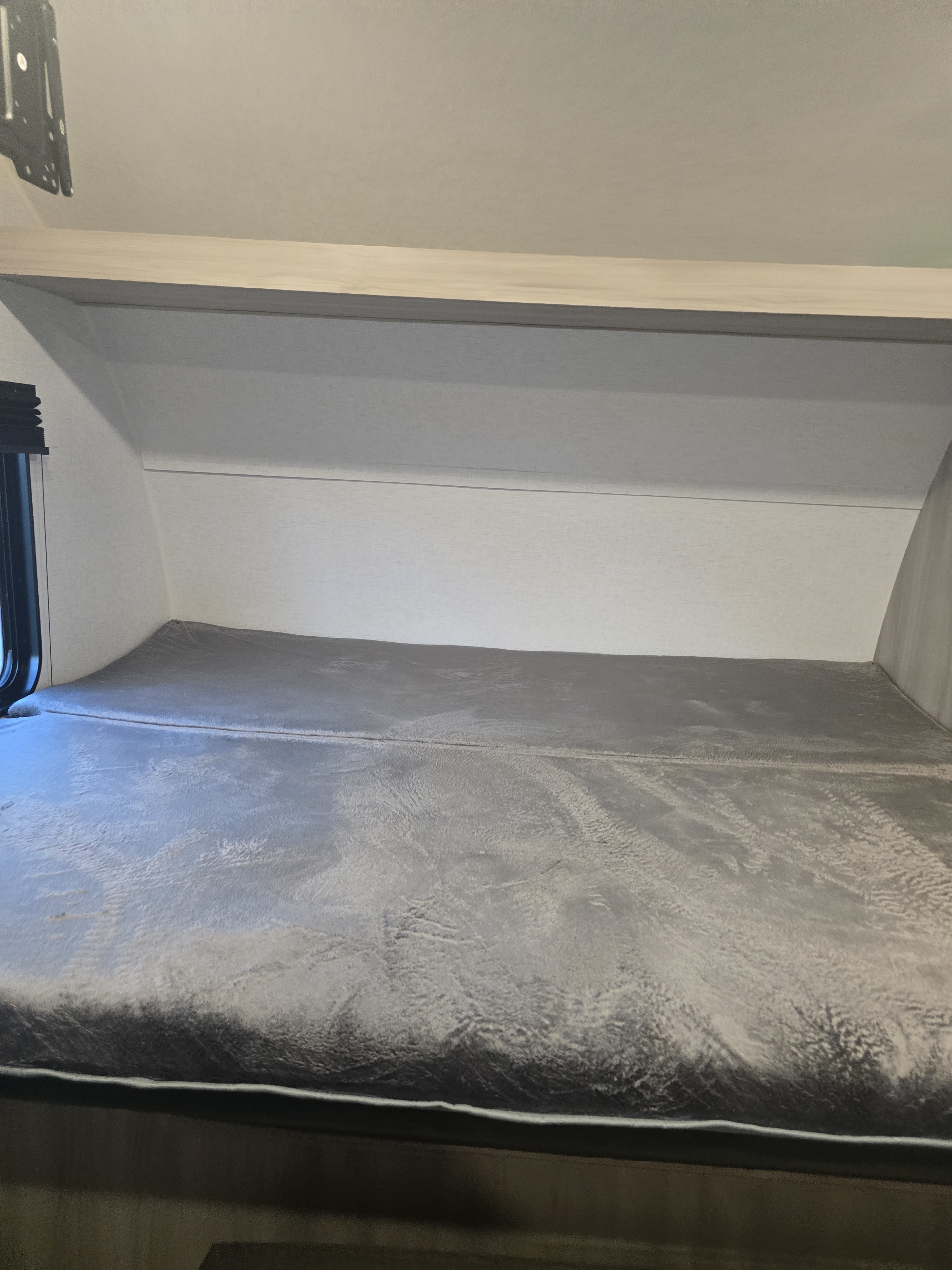 Comfortable gray bunk bed with a soft textured mattress inside an RV rental, ideal for travel and cozy sleeping.. East to West Silver Lake LE 2024