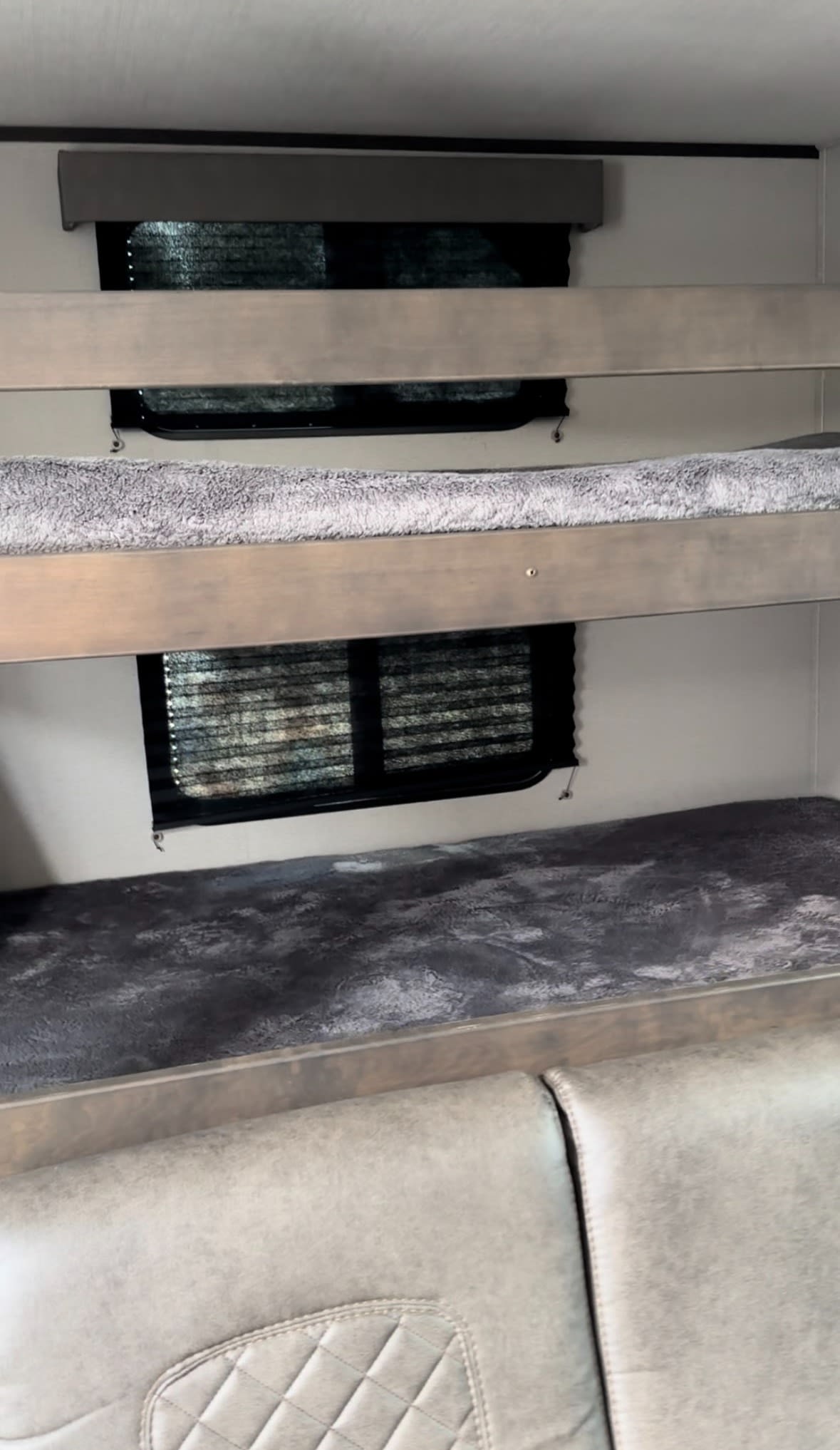 Inside an RV rental: two bunk beds with soft grey blankets, windows with blinds, and quilted cushioned seating below.. Grand Design Transcend Xplor 2023