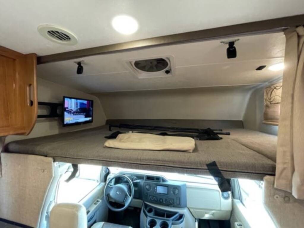 Inside this **rv rental**: an overhead bunk bed with TV and the driver's cab below, offering a cozy travel living space.. Coachmen Leprechaun 2019