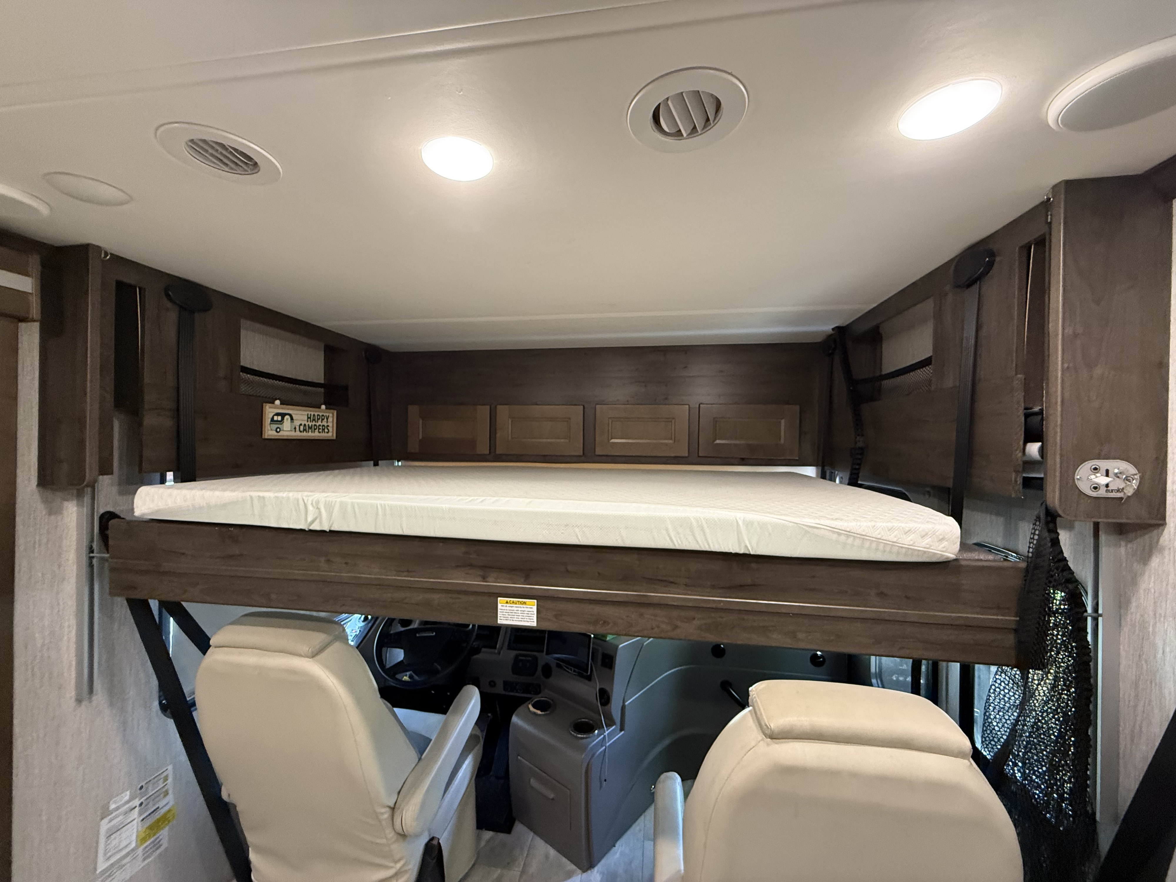 Inside an RV rental, a cozy cab-over bunk bed with a mattress is positioned above the driver's cabin, offering extra sleeping space.. Coachman Sports coach 2021