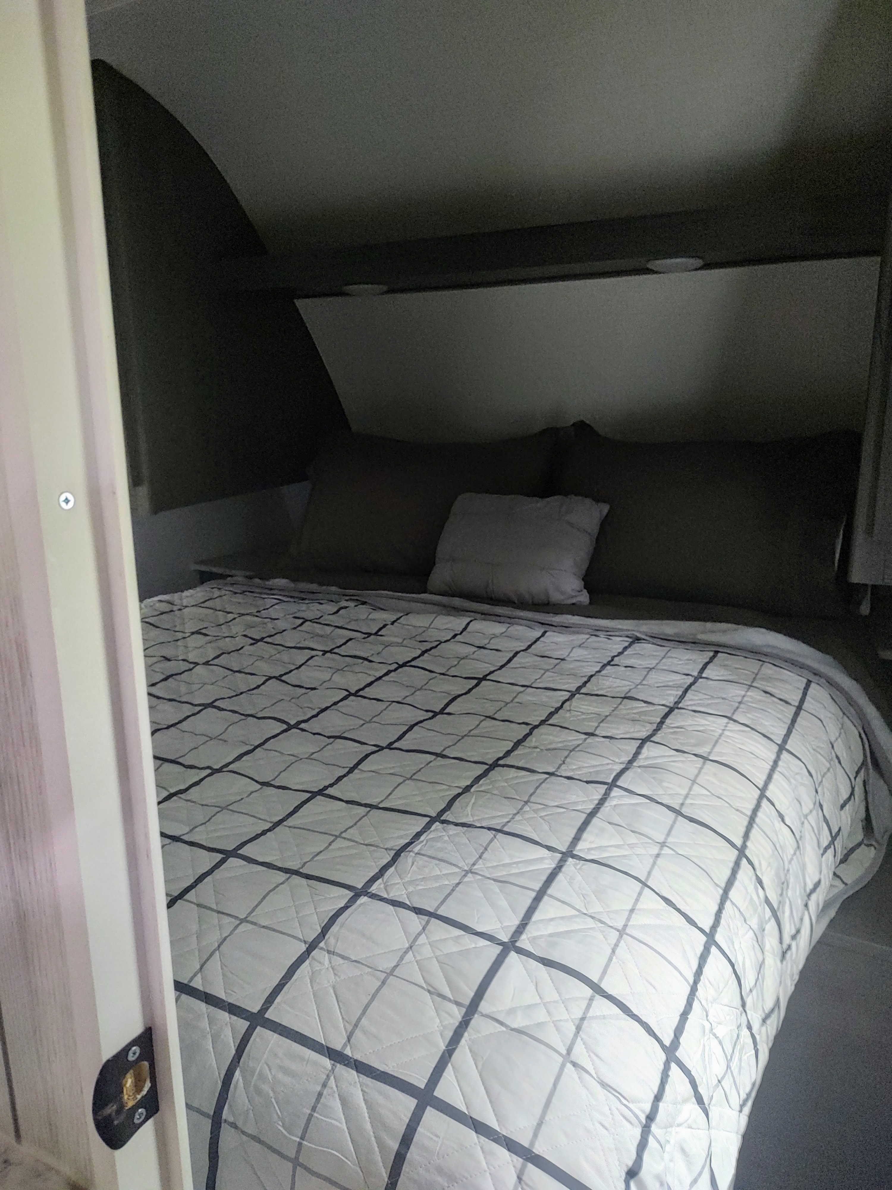 Inside an RV rental: a compact bedroom with a white grid-patterned comforter on the bed, dark pillows, and a light-colored headboard.. Dutchmen Colorado 26BHC 2024
