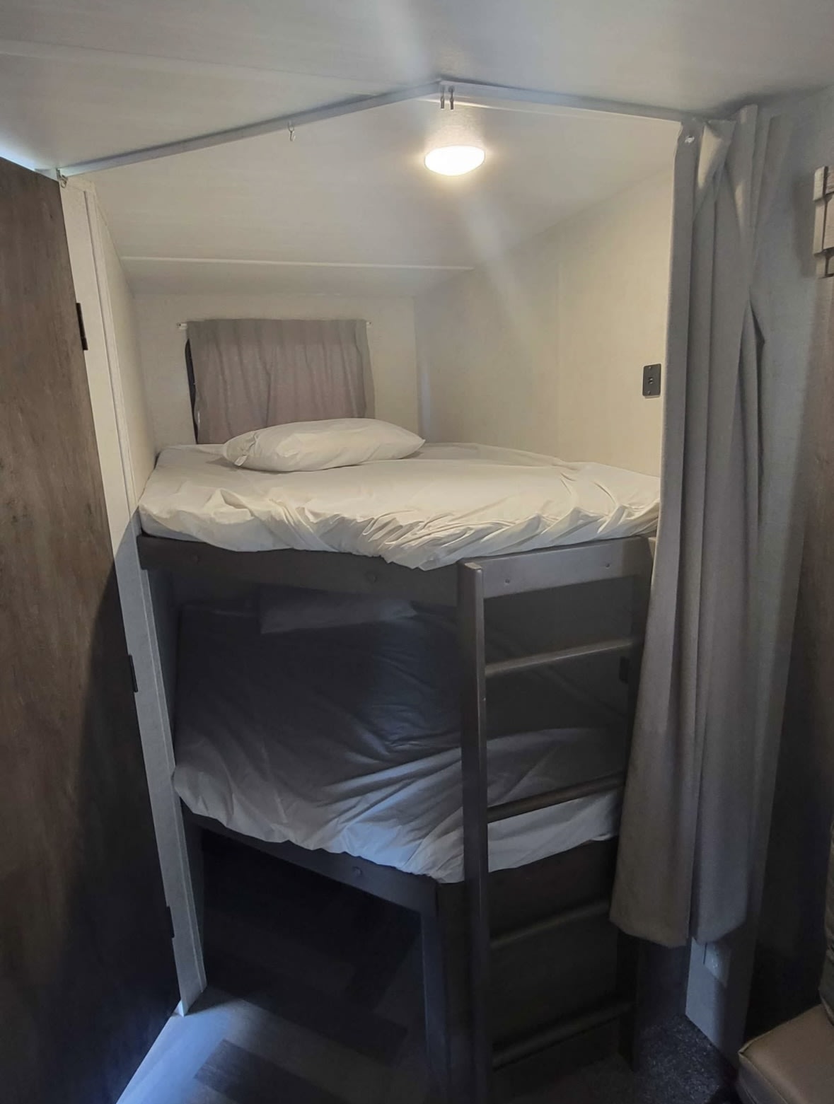 Cozy RV rental sleeping area featuring comfortable bunk beds with white sheets, a privacy curtain, and a window.. Forest River Wildwood 2021