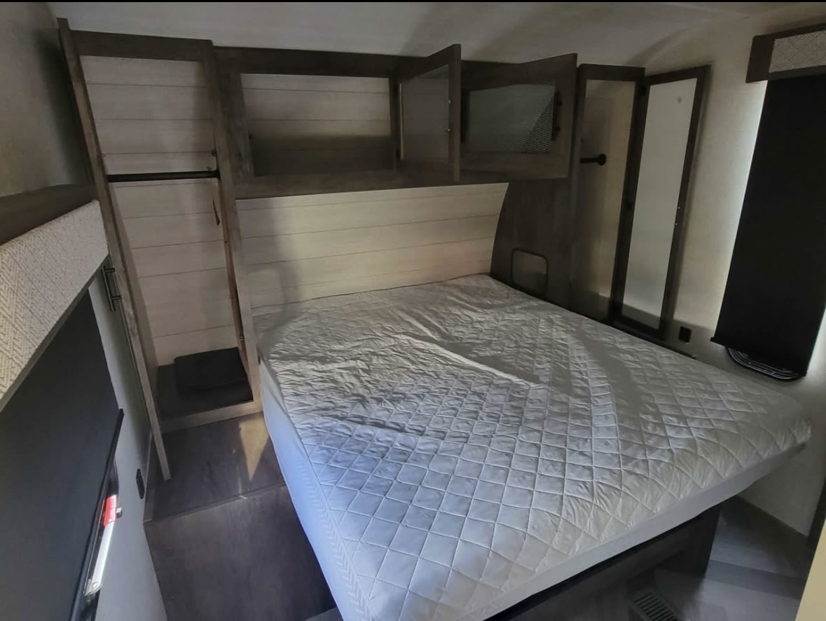 RV rental bedroom: Comfortably sized interior featuring a bed, ample built-in storage, and mirrored cabinet.. Forest River Wildwood 2021