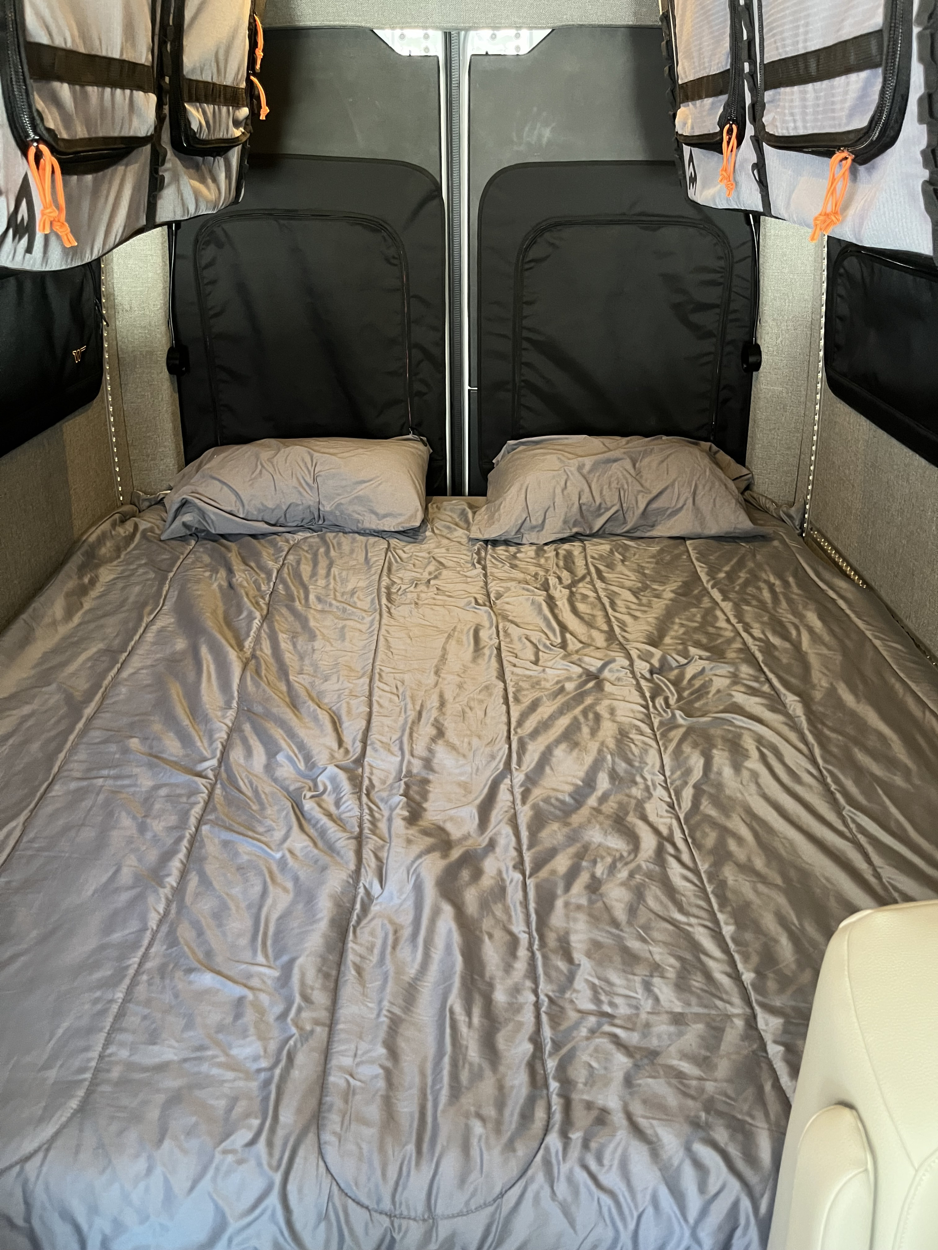 Spacious RV rental interior featuring a comfy bed with pillows, storage bags, and practical lighting.. Winnebago Adventure Wagon 2023