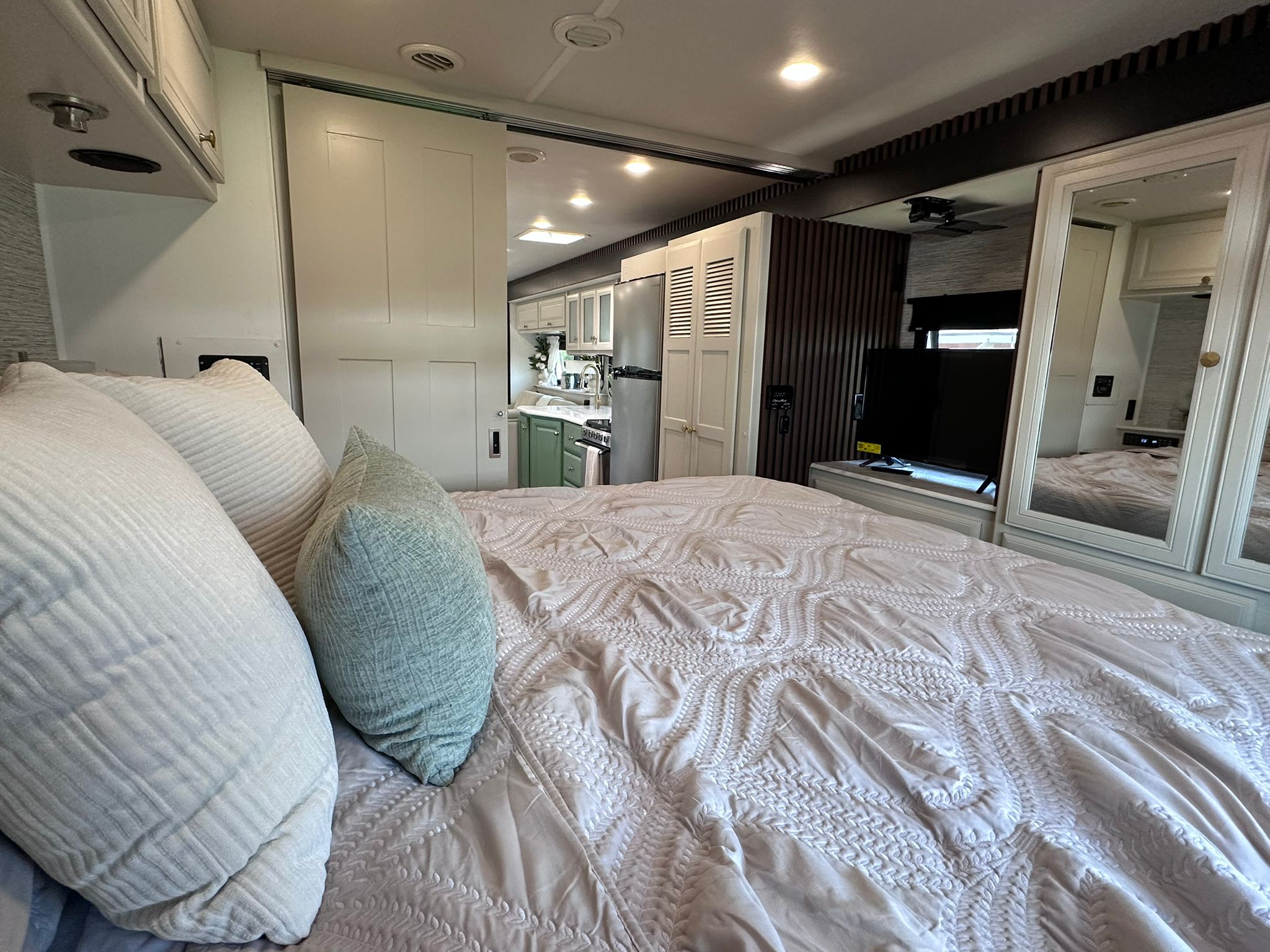 RV rental bedroom: a cozy space with quilted comforter, mirrored storage, and sliding door to a modern kitchen area.. Fleetwood Flair 2021