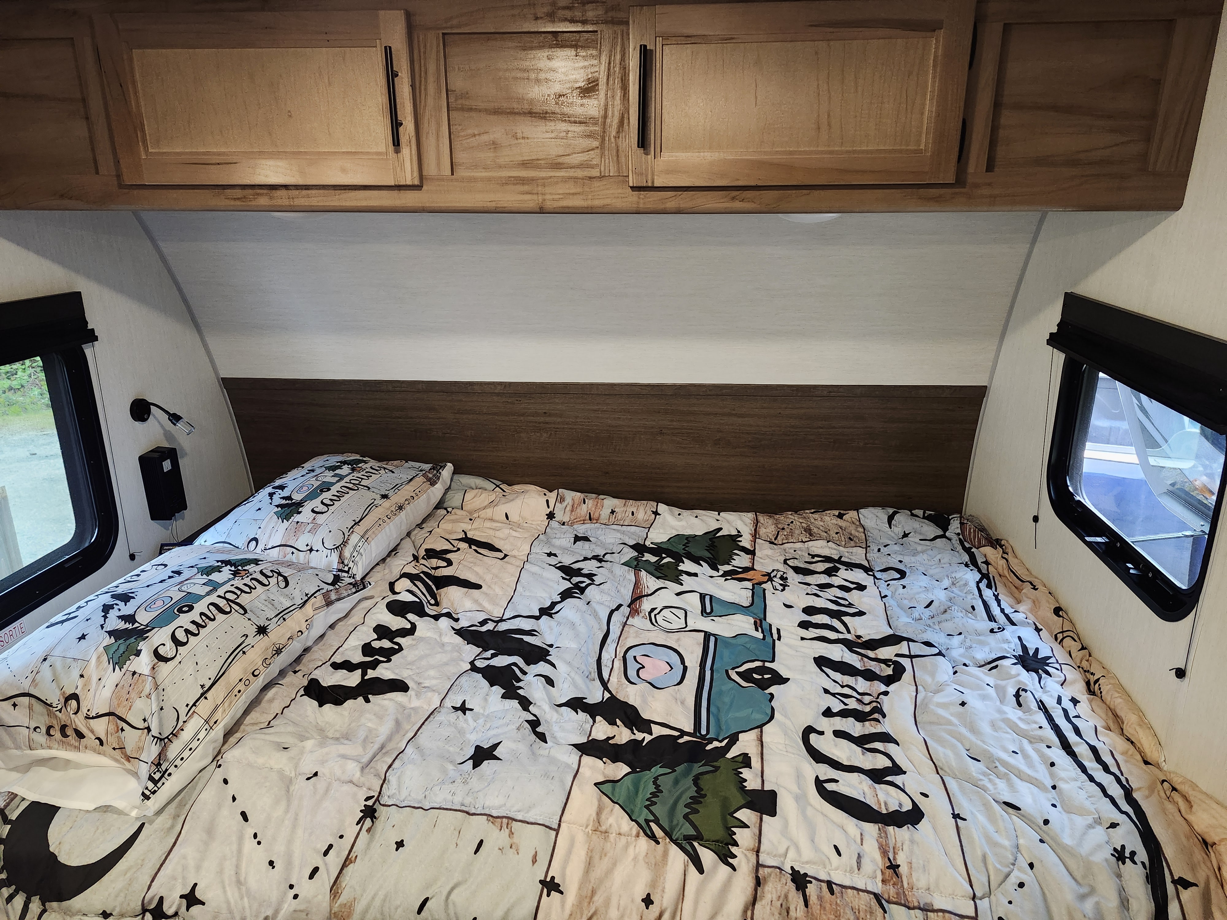 Comfortable RV rental bedroom with camping-themed bedding, overhead cabinets, and side windows.. Forest River Cherokee Black Label 2025