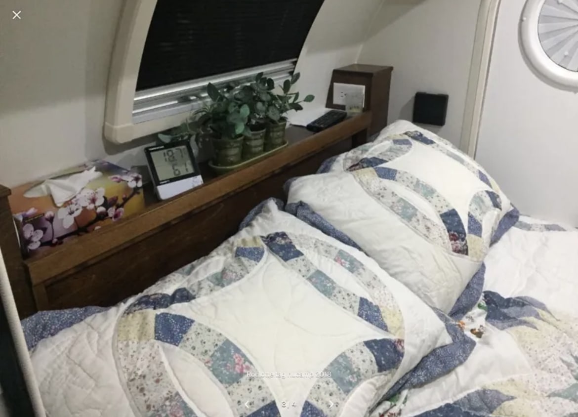 RV rental bedroom: cozy bed with quilted pillows, shelf with tissues & temperature display, and window.. nuCamp T@G 2018