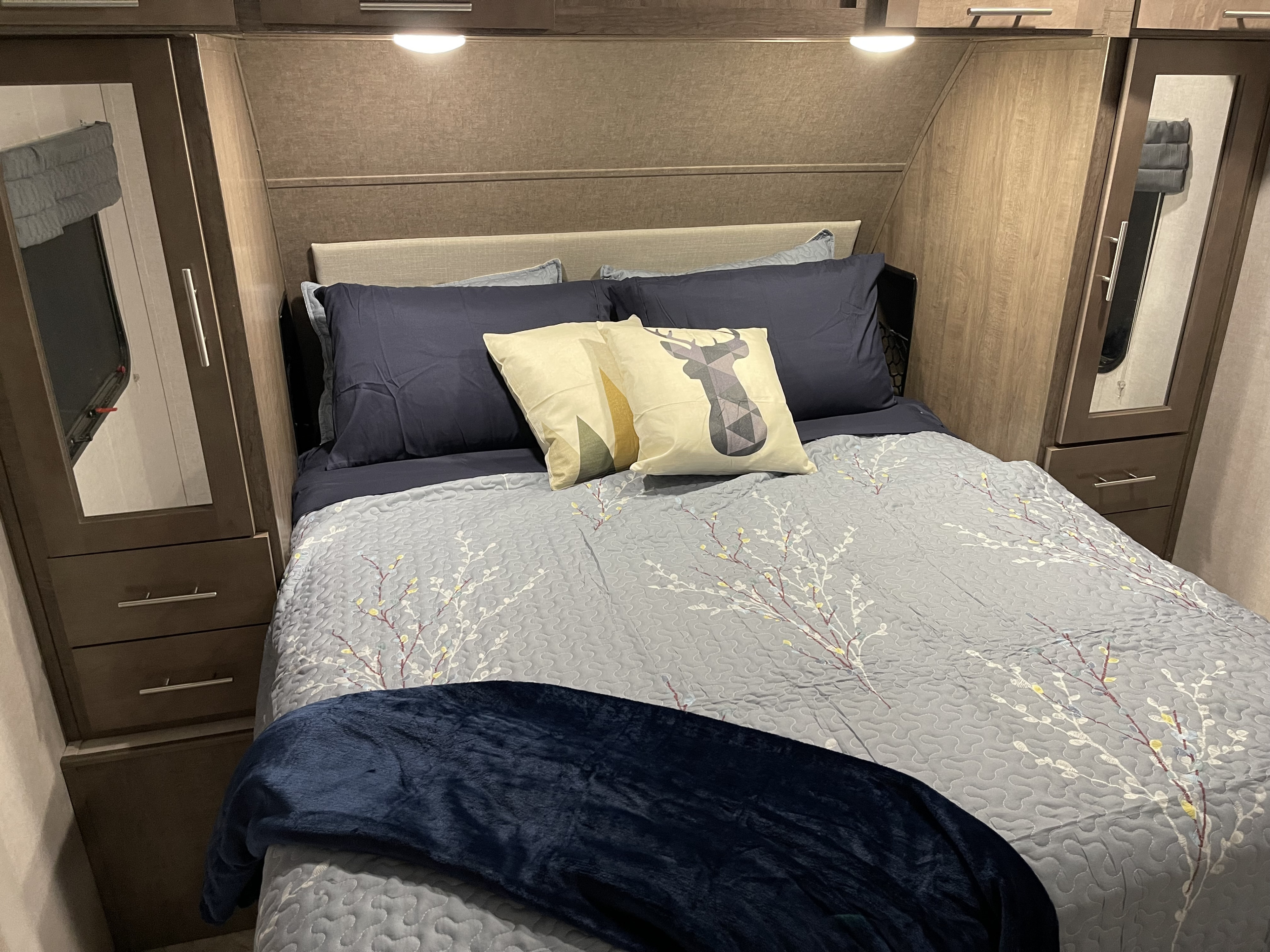 Cozy RV rental bedroom with a neatly made bed, blue bedding, patterned quilt, and wooden mirrored cabinets.. Forest River Surveyor 2018