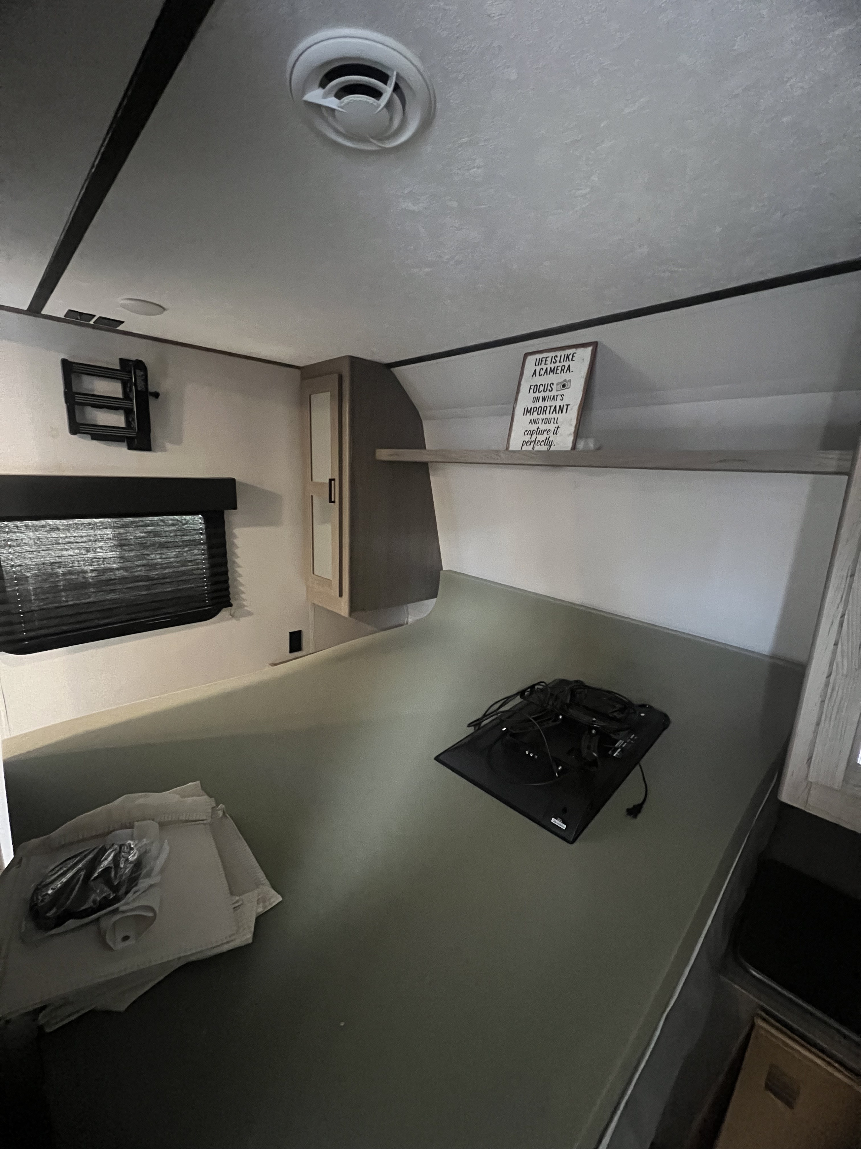 This RV rental bedroom features a grey mattress, window, TV wall mount, and overhead cabinet. Ideal for a comfortable stay.. Keystone RV Hideout 2021