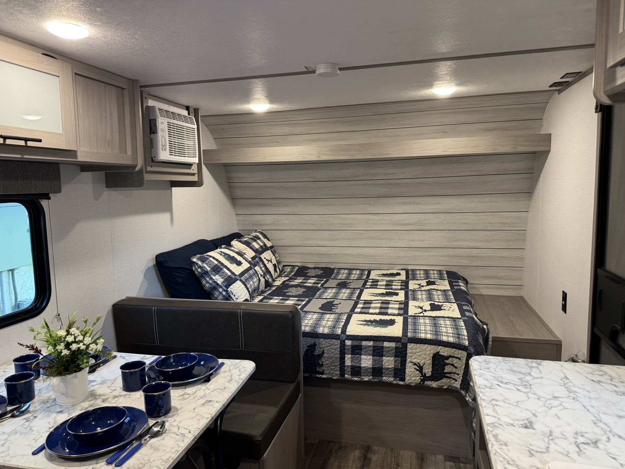 Inside a modern RV rental: a comfy bed with patterned quilt, dining table set for four, and compact amenities.. Dutchman Coleman Lantern LT 2024