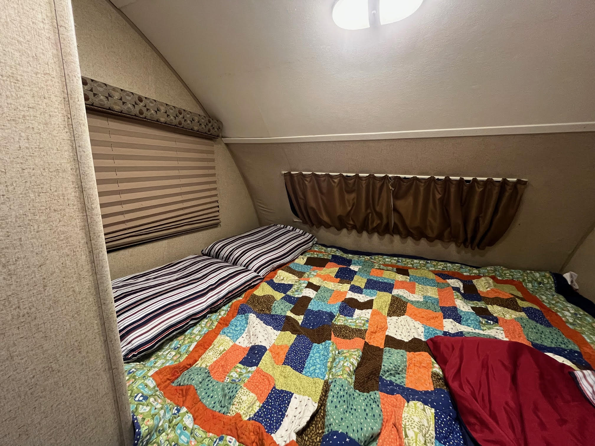 Inside a cozy RV rental bedroom: a colorful quilt, striped pillows, and functional window treatments. Ideal for travel.. R-Pod R-Pod Trailer 2015