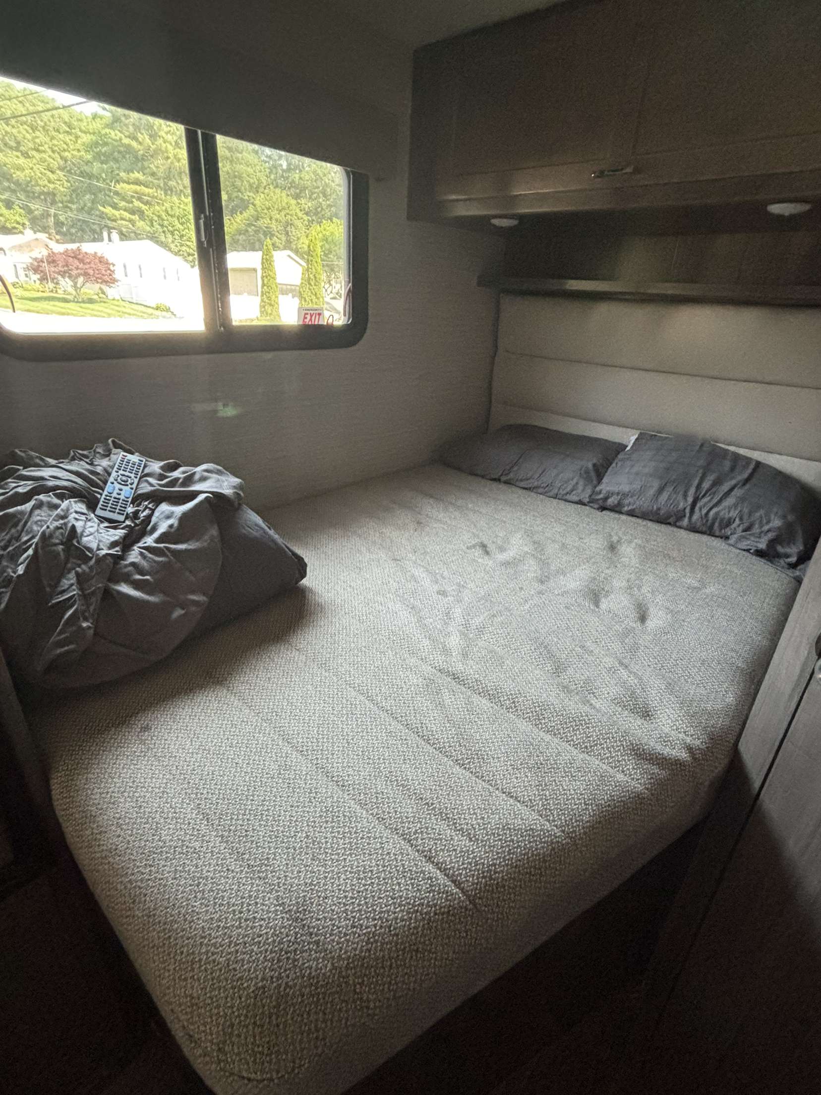 Step inside this RV rental bedroom featuring a comfy bed, overhead storage, and a large window showing an 'EXIT' sign outside.. Winnebago Minnie Winnie 2022