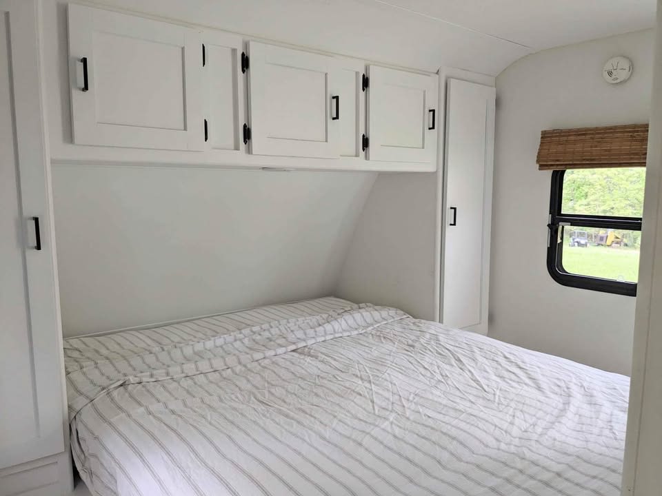 This bright RV rental bedroom features white cabinets, striped bedding, and a window with a natural blind.. Keystone RV Passport Grand Touring 2014