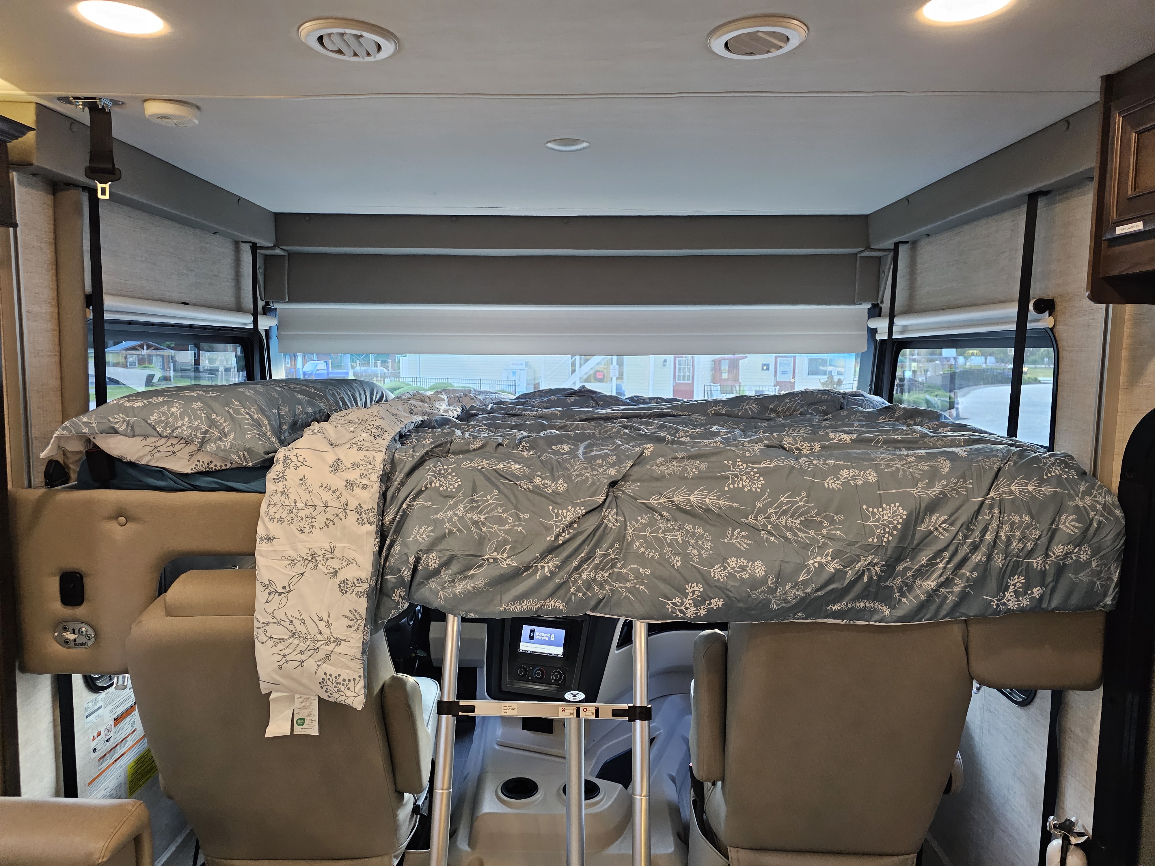 An RV rental's comfy bunk bed setup above the driver's area. Features windows with a street view and overhead lighting.. Entegra Coach Vision XL 2022