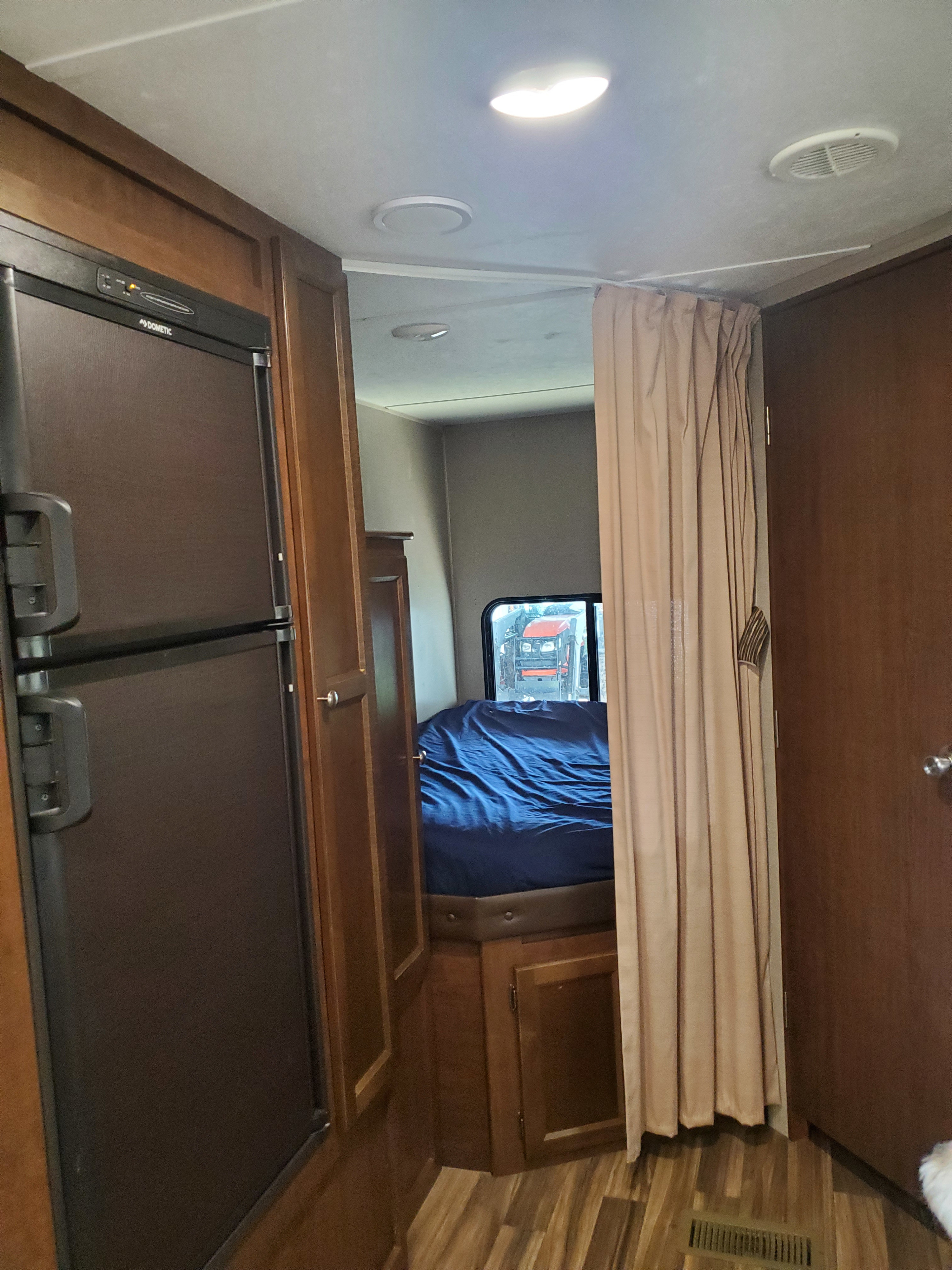 Bright RV rental interior with a Dometic refrigerator, wood-toned cabinets, and a curtained bedroom area with a bed.. Keystone RV Hideout 2018