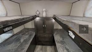 This rv rental bunk bed interior features four beds with dark bedding, and a central storage cabinet, providing a family sleeping area.. Forest River Surveyor Legend 2021