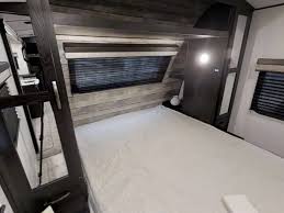 Inside this RV rental bedroom: a large bed, bunk area, windows with blinds, and wood-look walls. A cozy, practical space.. Forest River Surveyor Legend 2021