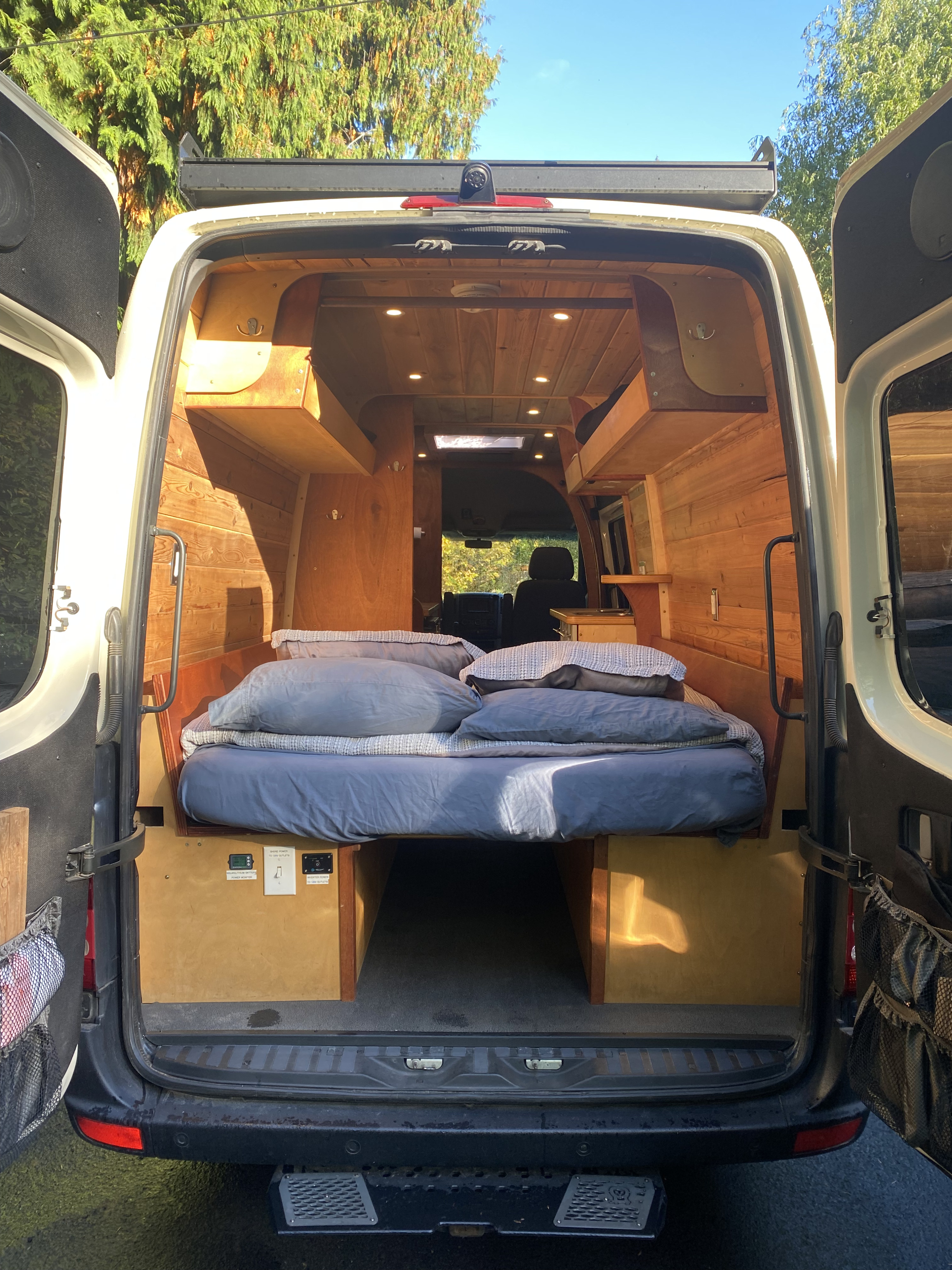Rear view of a custom RV rental camper van, featuring a comfy bed, wood interior, and built-in amenities for travel comfort.. Mercedes-Benz Sprinter 2008