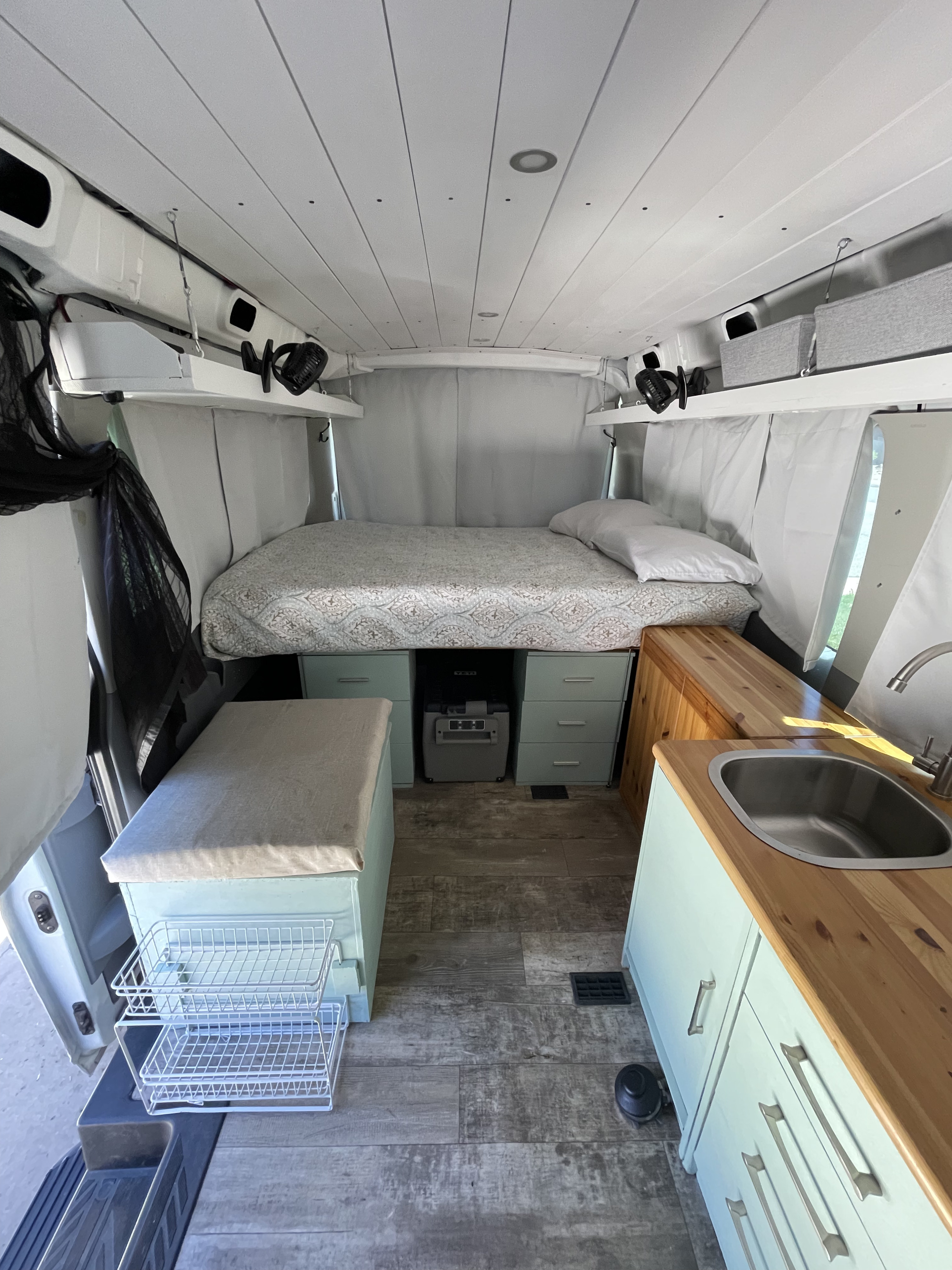 Inside an RV rental: a modern camper van with bed, light blue kitchen, wood floors, and ample storage.. Ford Transit Custom 2017