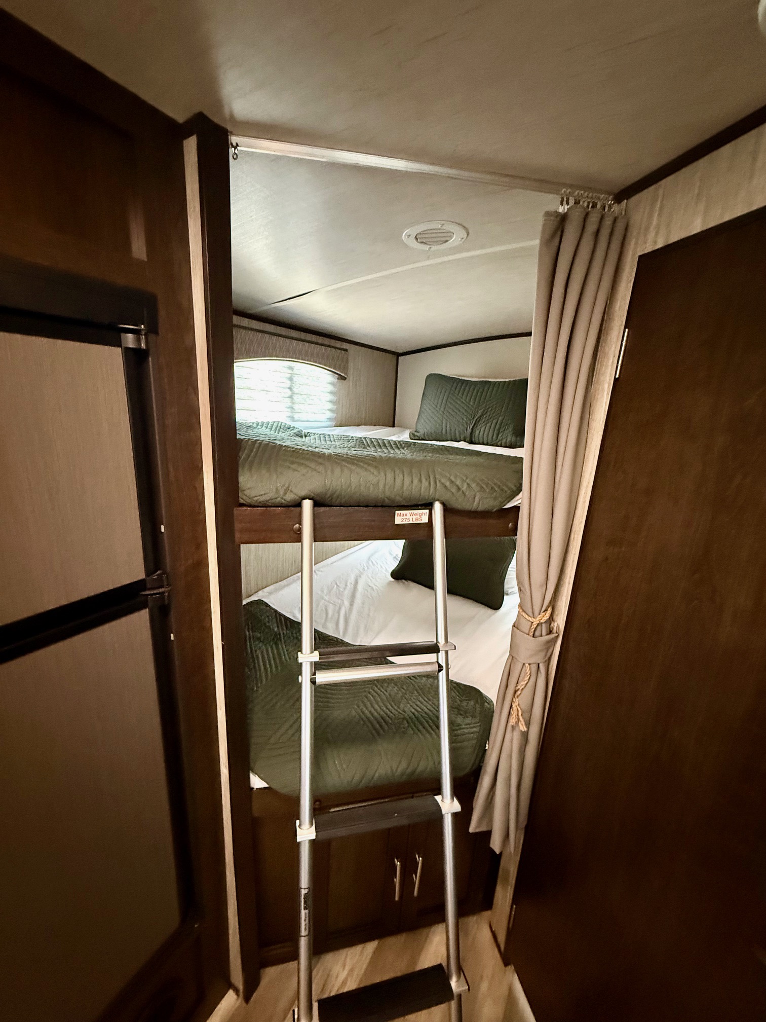 RV rental bunk beds with green bedding, ladder, and privacy curtain, ideal for compact sleeping in a travel trailer.. Cruiser RV Fun Finder Xtreme Lite 2019