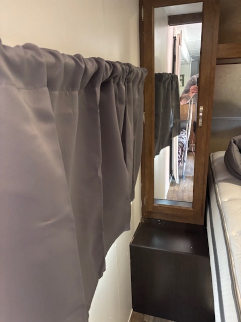 Compact interior of an RV rental: grey curtain, mirrored cabinet, and bedside area. Reflected person uses a crutch.. Forest River Salem Cruise Lite 2017
