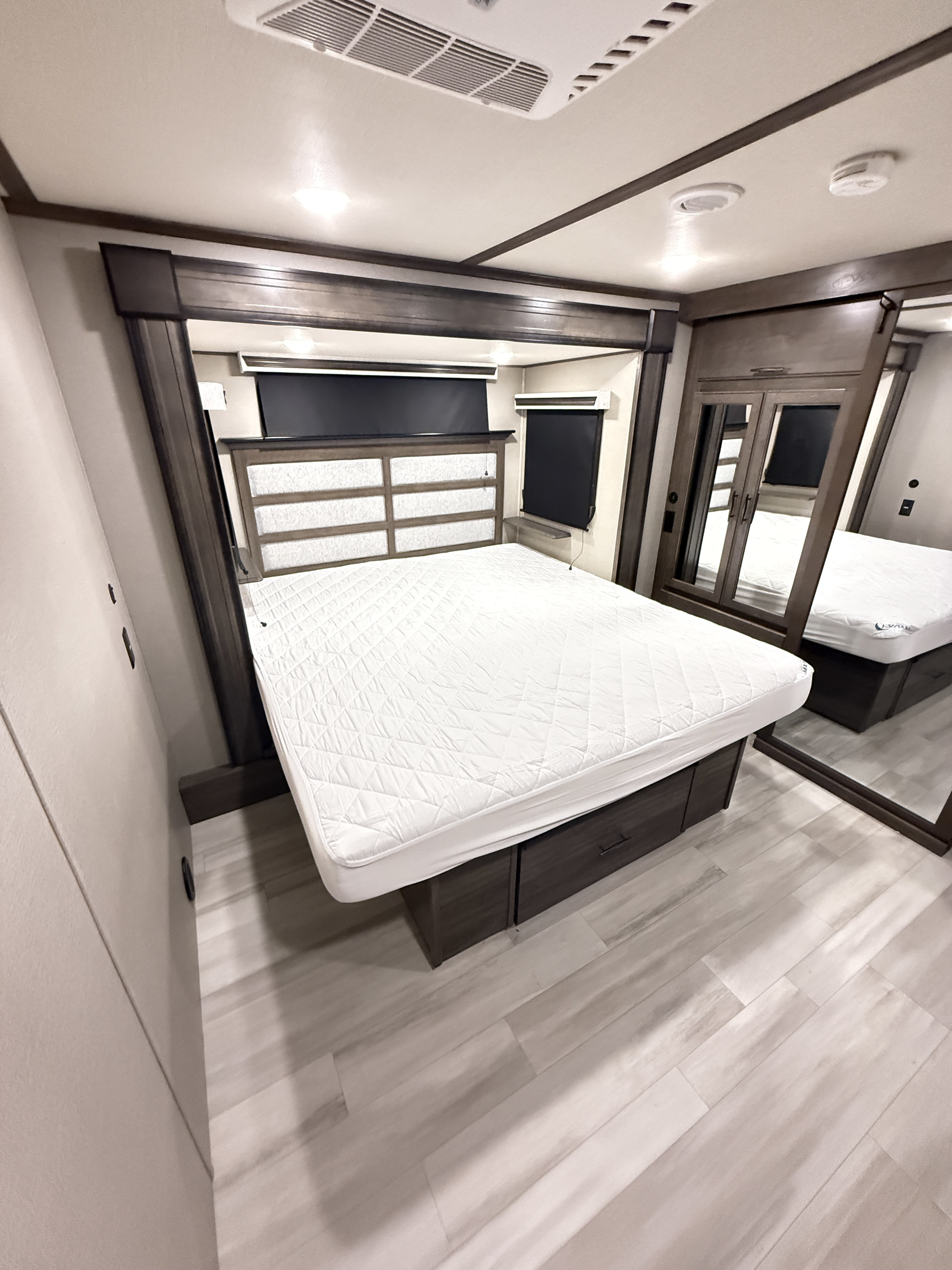 Inside a comfortable RV rental bedroom, featuring a large bed with storage, sleek shades, and a mirrored wardrobe.. Grand Design Solitude 2022