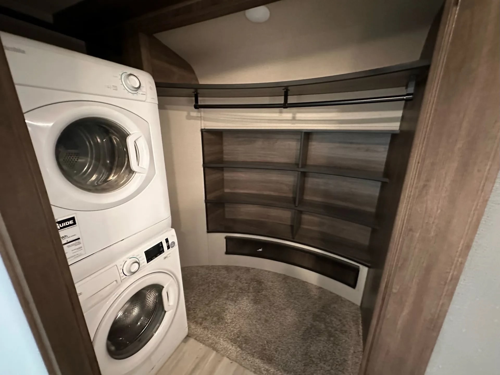 Compact RV rental closet: stacked washer/dryer, curved shelves, and hanging rod for organized living on the road.. Grand Design Solitude 2021