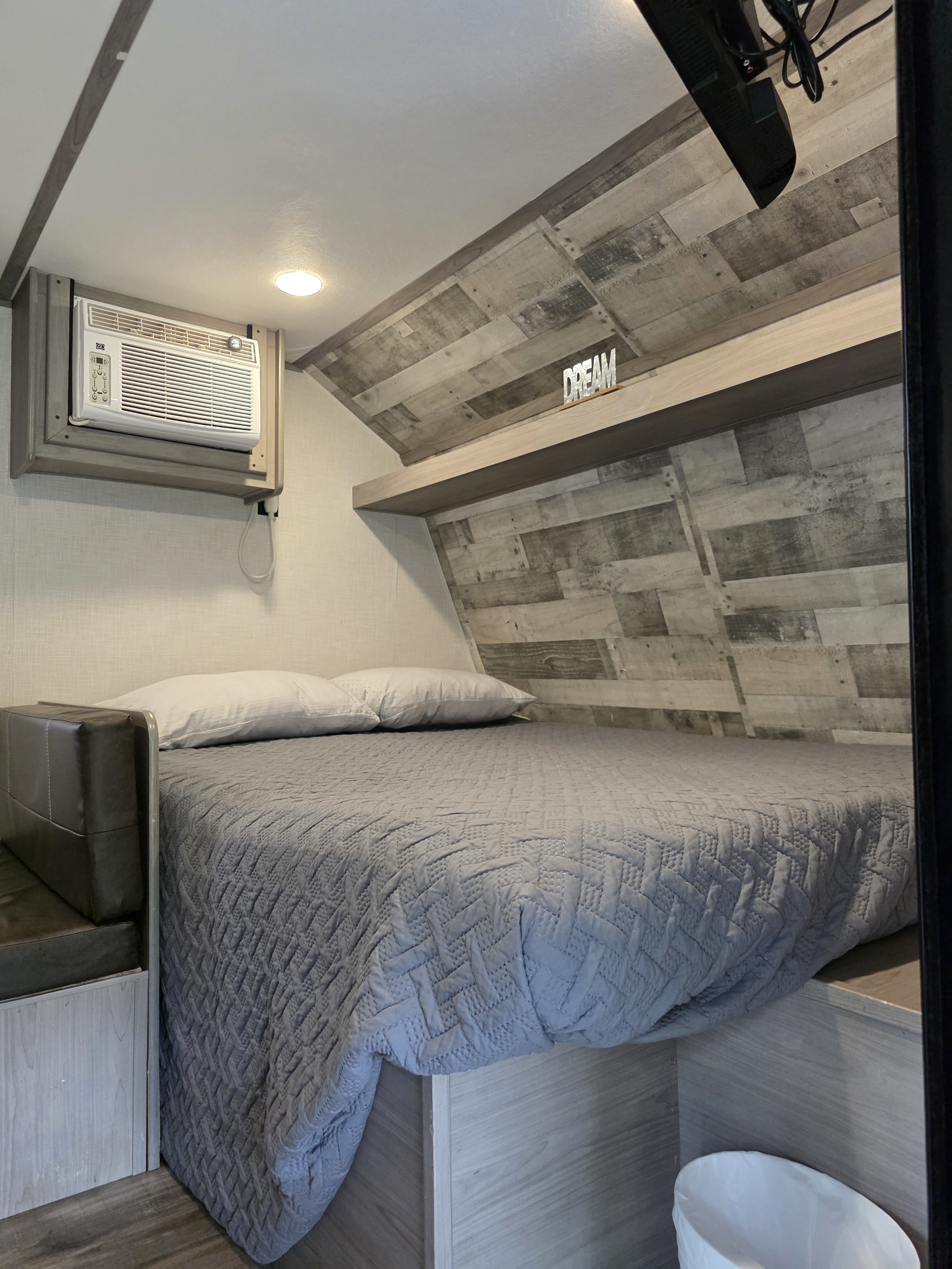 Comfortable RV rental bedroom with a quilted bed, mounted AC unit, and stylish wood-look wall panels.. Dutchmen Coleman Lantern LT 2022