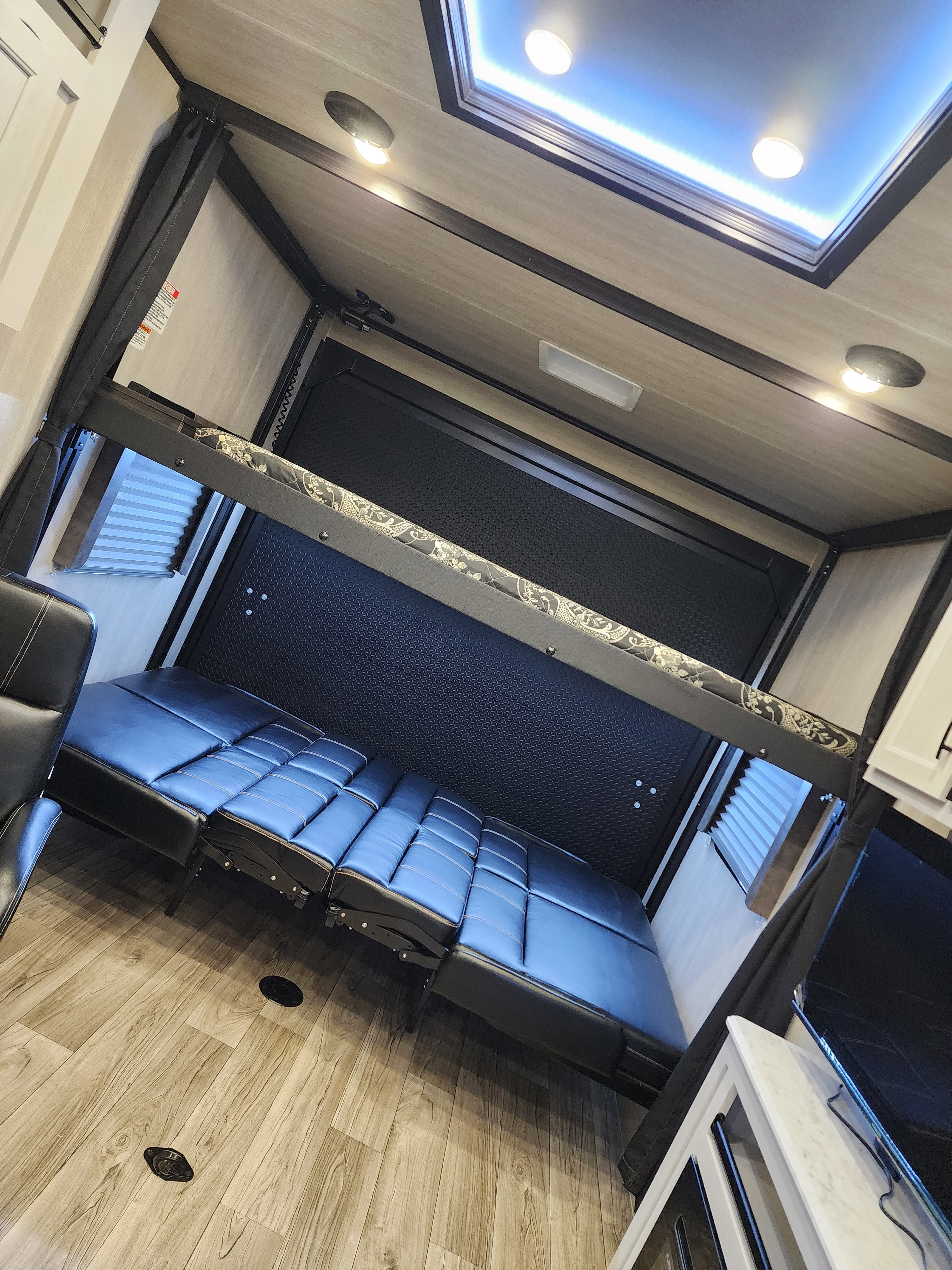 Bright RV rental interior features wood-look flooring, versatile convertible sofas, and an elevated bunk bed.. Genesis Supreme Rv Genesis Supreme 2025