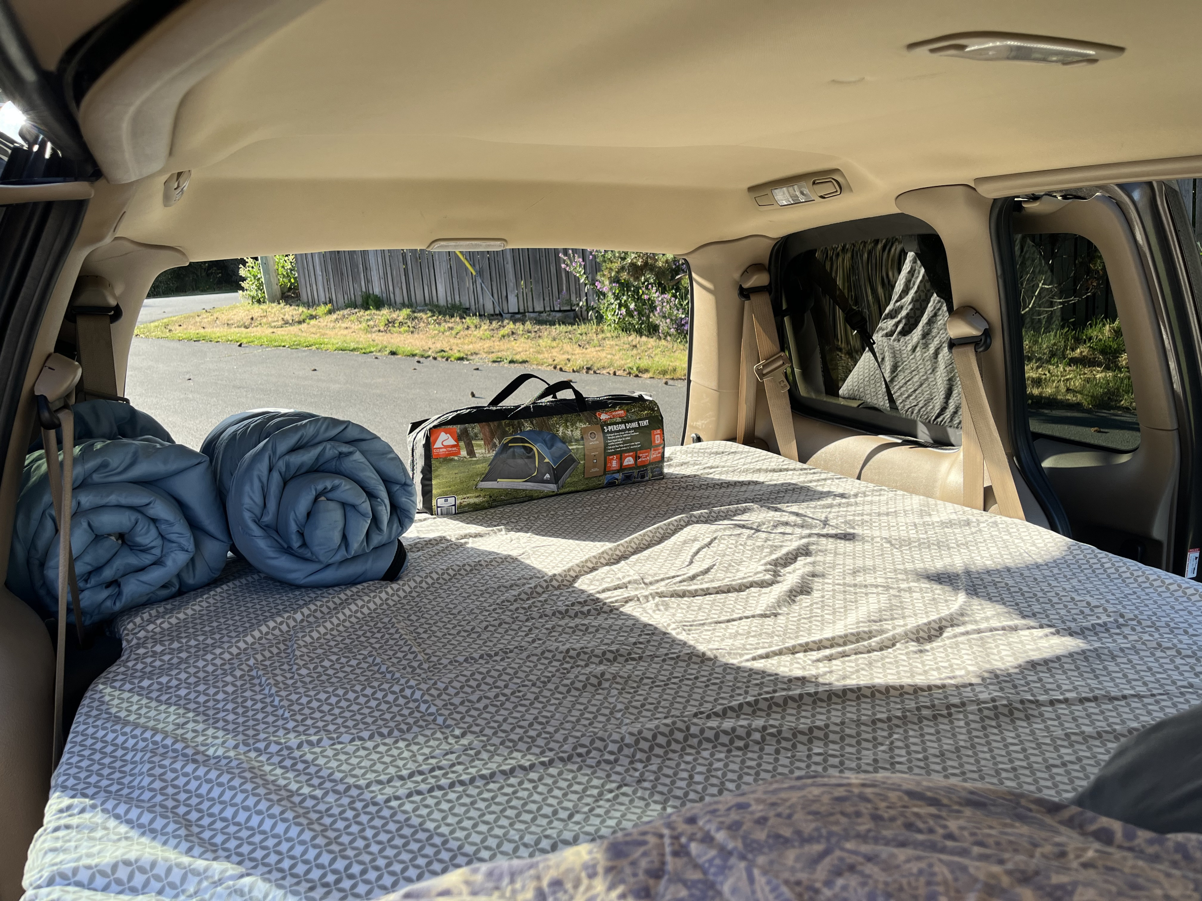 Inside a comfortable car camping setup with a bed, rolled sleeping bags, and a tent box. An easy RV rental alternative.. Chevrolet Uplander 2009