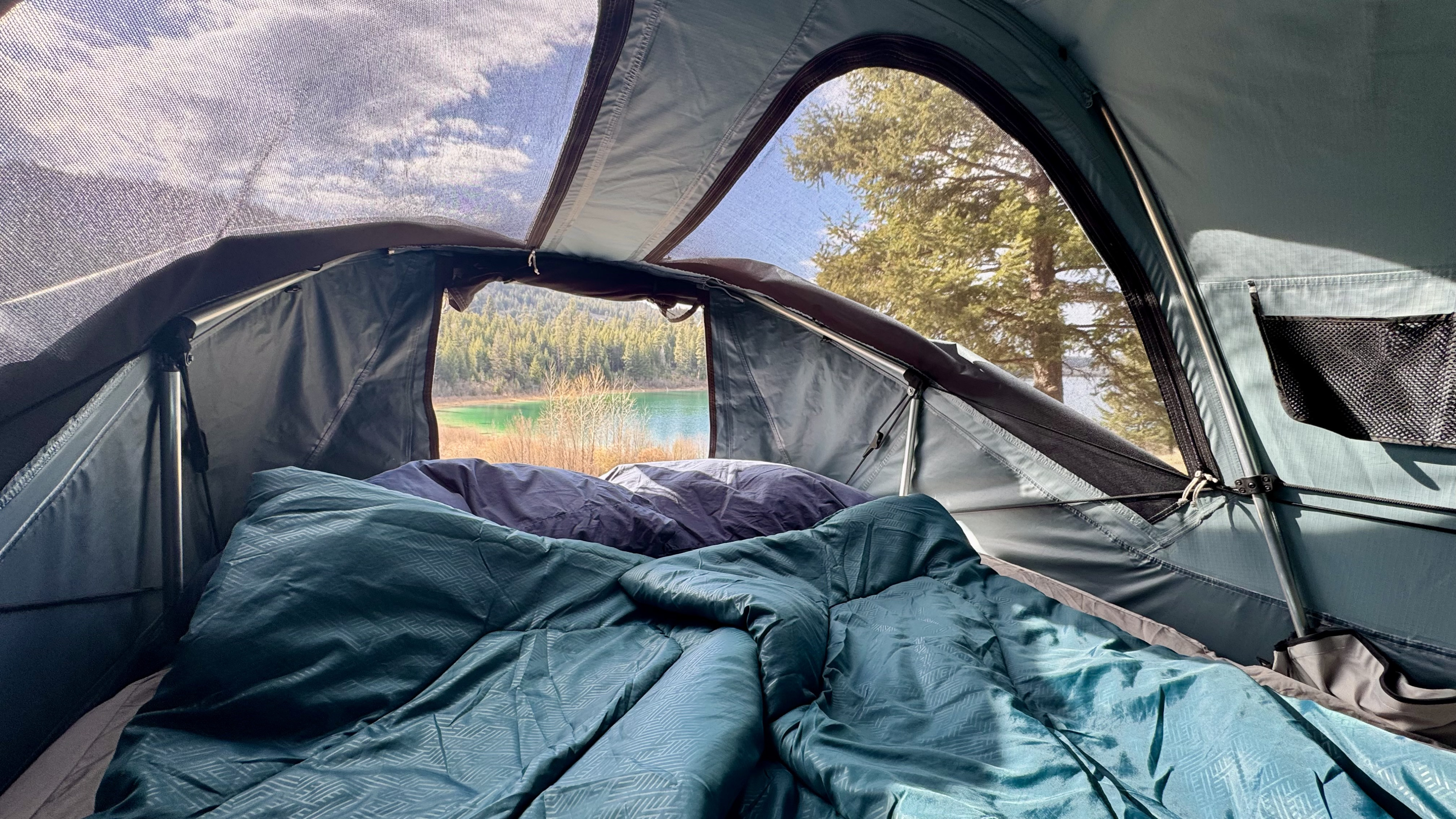 Cozy view from inside an RV rental rooftop tent, looking out at a scenic lake and forest.. Ford Maverick 2025
