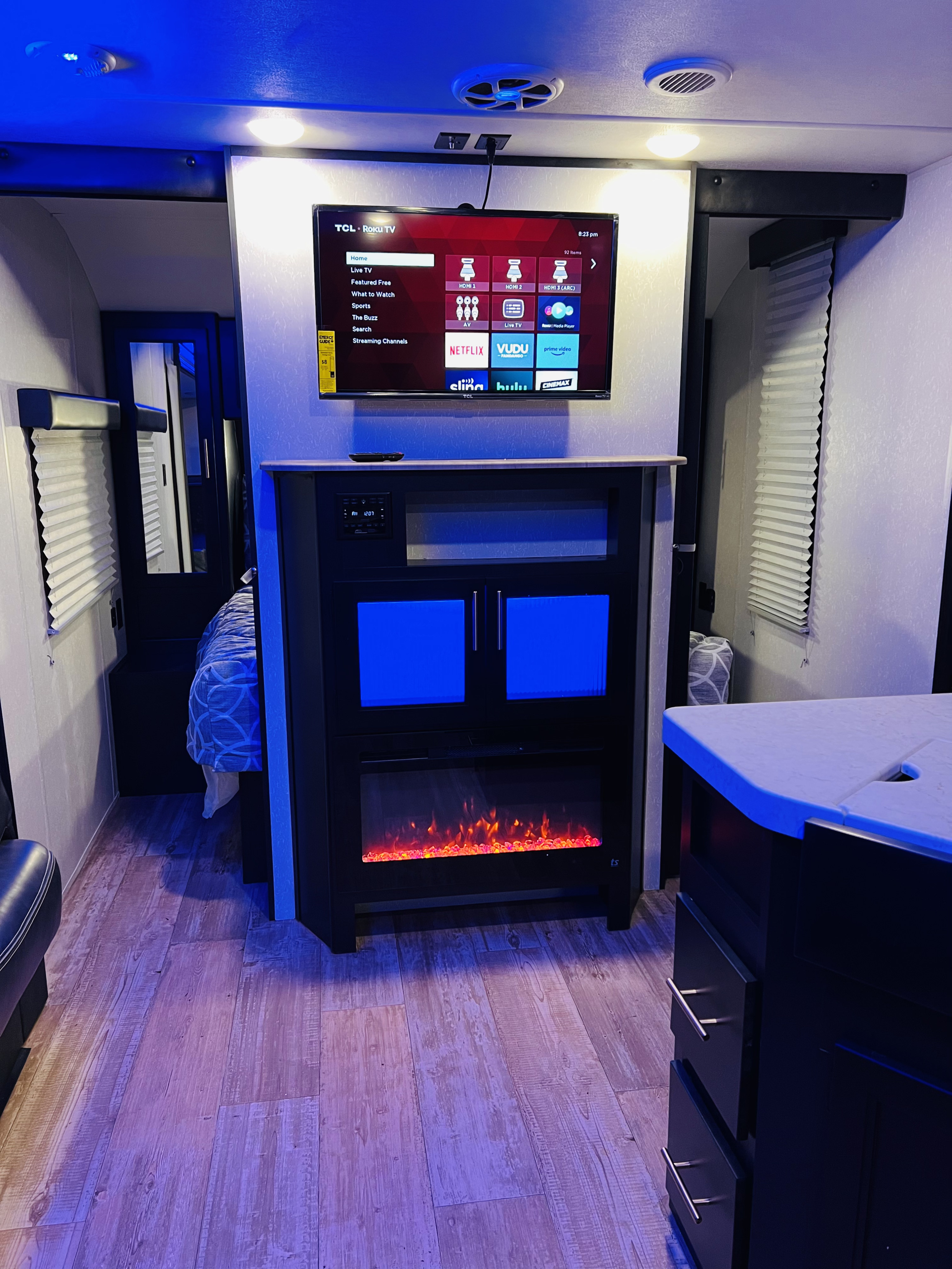 RV rental interior featuring a TV, electric fireplace, and kitchen island, all bathed in blue accent lighting.. Forest River Cherokee Grey Wolf 2021