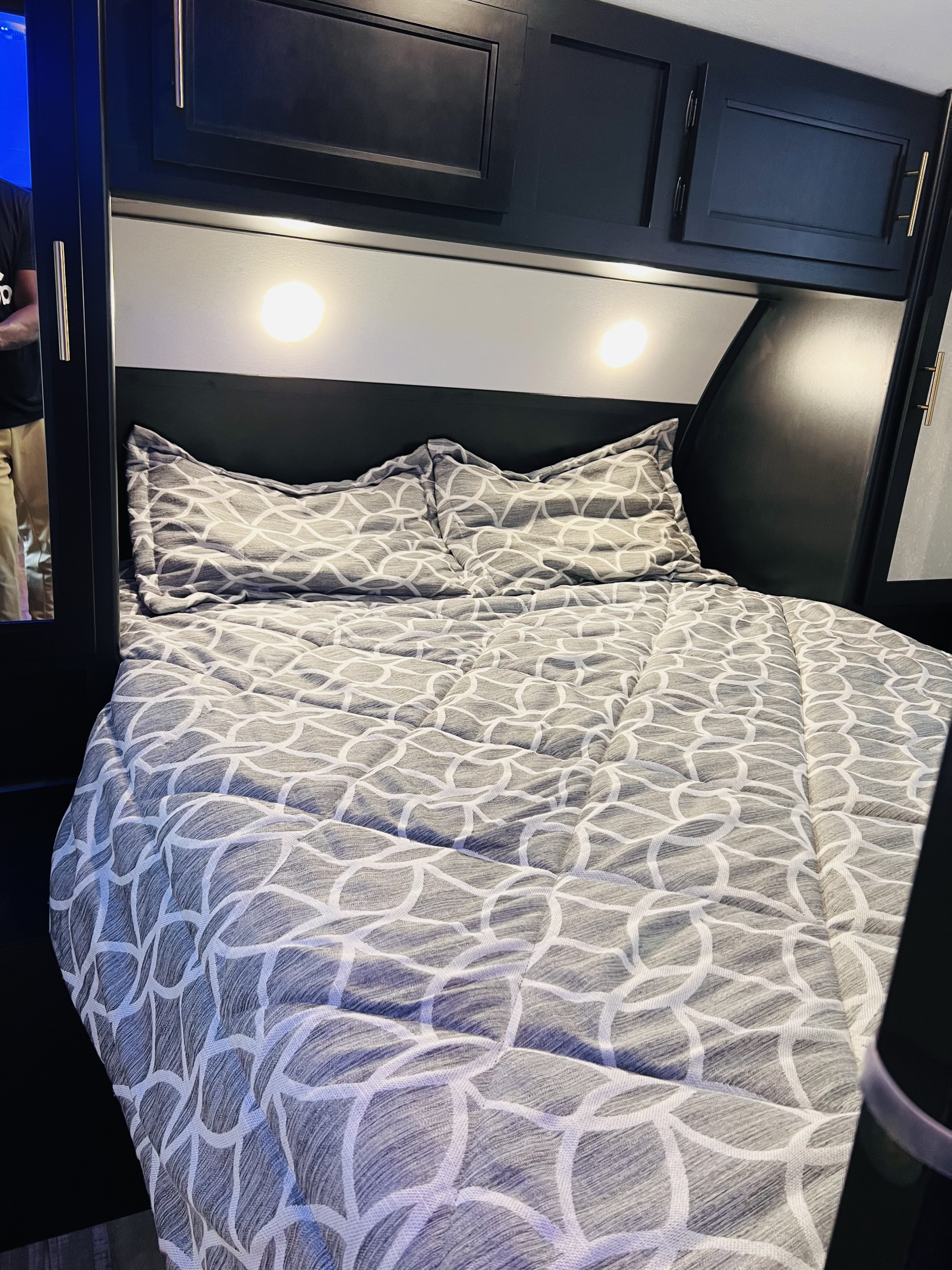 Cozy RV rental bedroom with a grey patterned bed, two pillows, and dark overhead cabinets, offering comfort on the road.. Forest River Cherokee Grey Wolf 2021